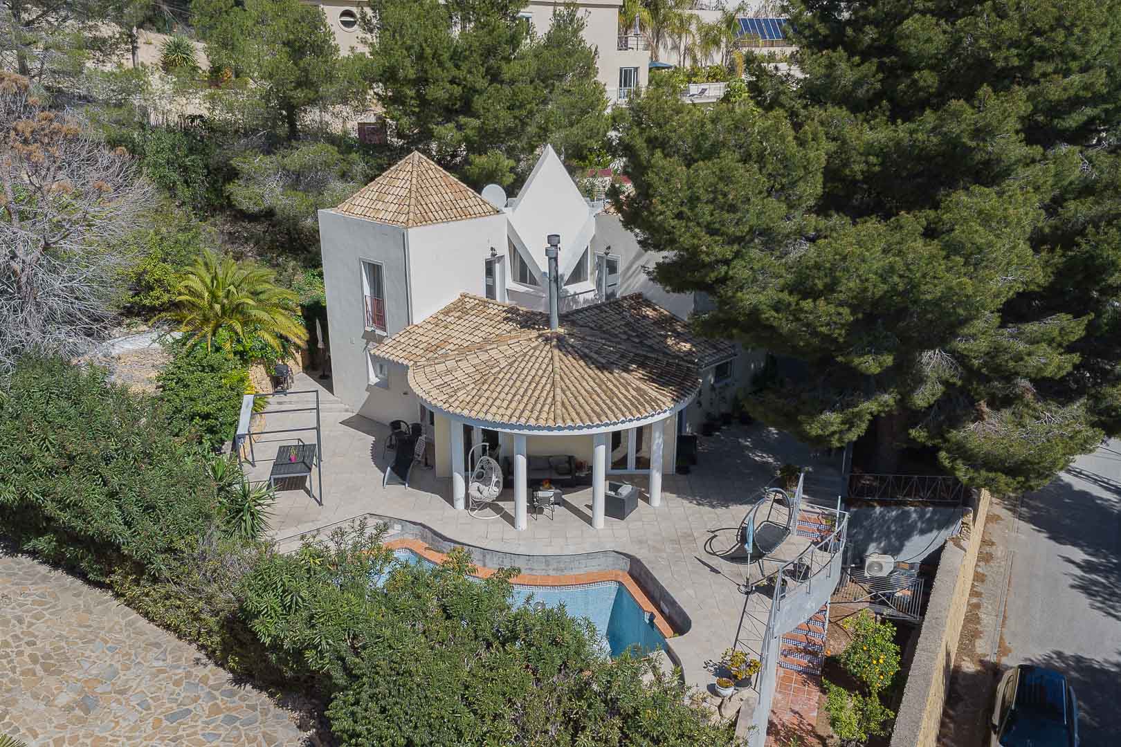 Luftaufnahme der Villa mit kreisförmiger Veranda, weißen Säulen, privatem Pool und Steinterrassen, eingebettet in einen Garten mit Pinien und Palmen.