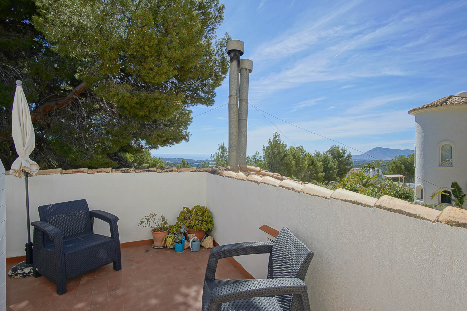 Obere Terrasse mit Terrakottaboden und Korbsesseln, die einen weiten Blick auf das Mittelmeer und die umliegende Pinienlandschaft bietet.