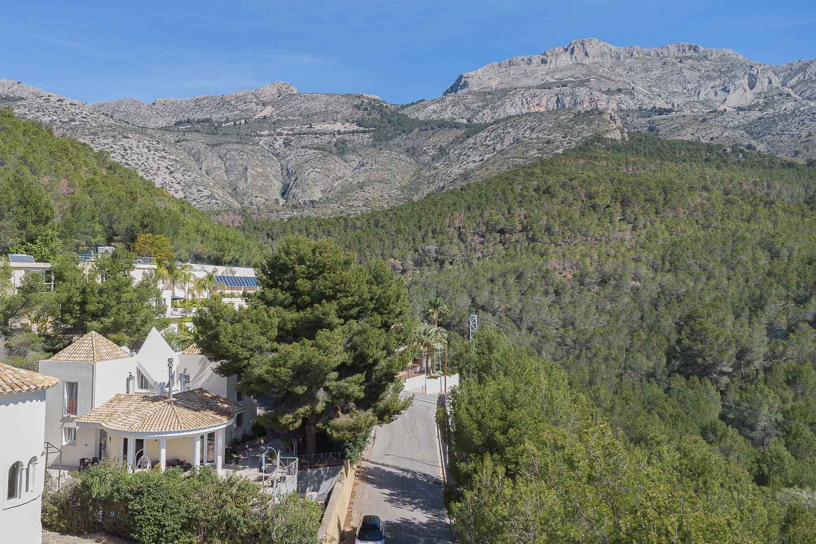 Panoramablick auf die in die Natur eingebettete Villa, die ihre mediterrane Architektur vor einem dichten Pinienwald und der majestätischen Bergkette zeigt.