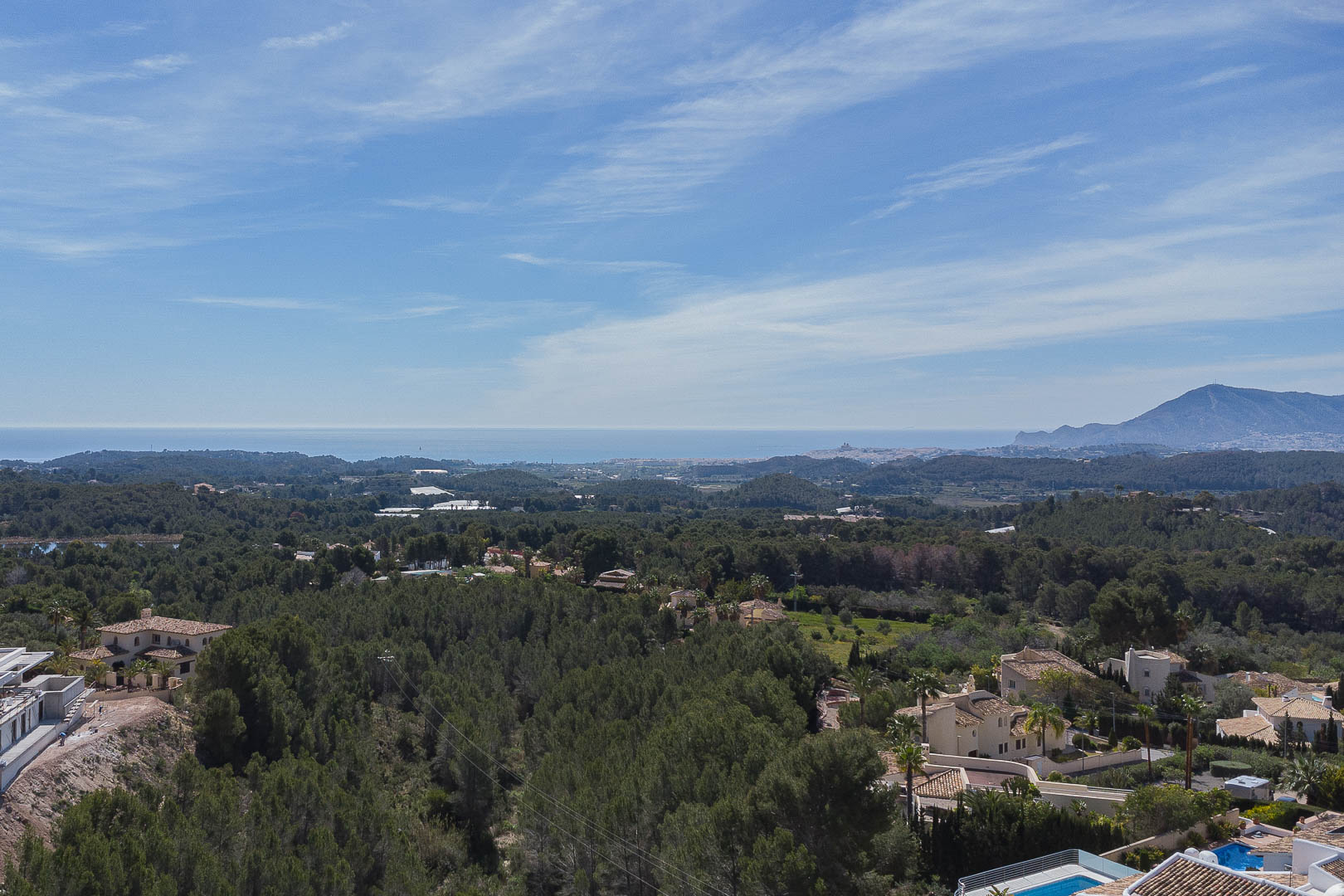Panoramablick von der oberen Terrasse über einen dichten Pinienwald, die Mittelmeerküste am Horizont und die Bergsilhouetten unter klarem Himmel.