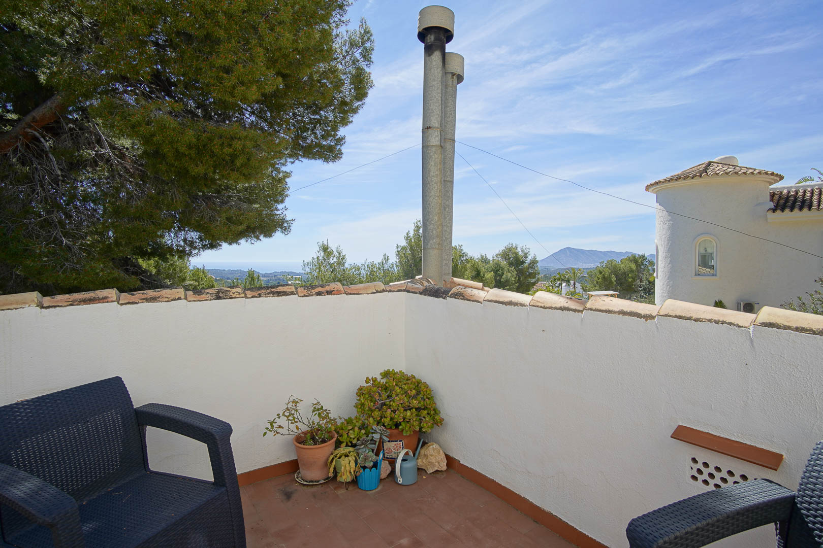 Terrasse im Obergeschoss mit Terrakottaboden, Außenmöbeln und weitem Blick auf das Meer und die Berge in waldreicher Umgebung.