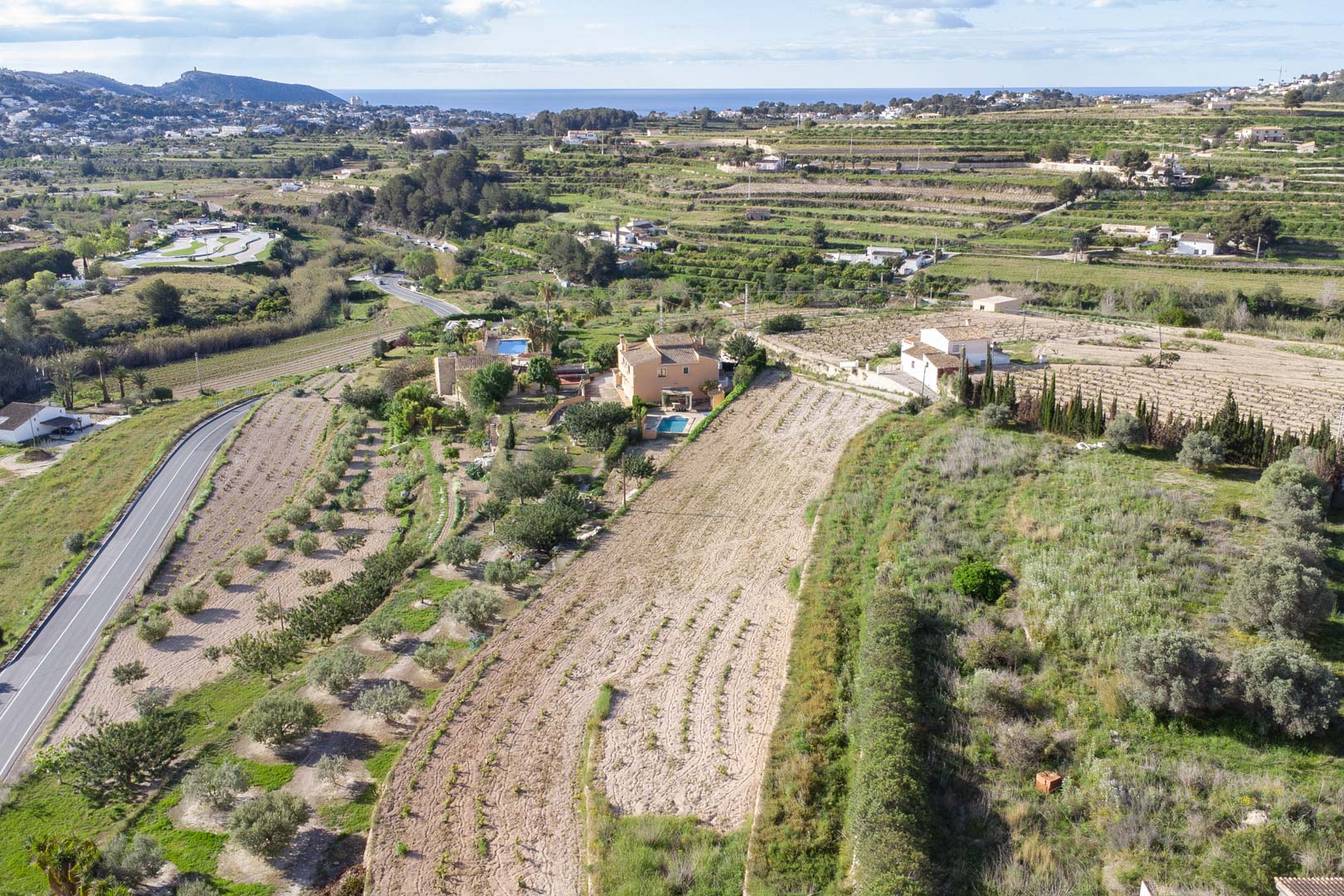 Luftaufnahme des 10.920 m2 großen Grundstücks in Teulada-Moraira mit terrassierten Flächen und Panoramablick auf die Mittelmeerküste.