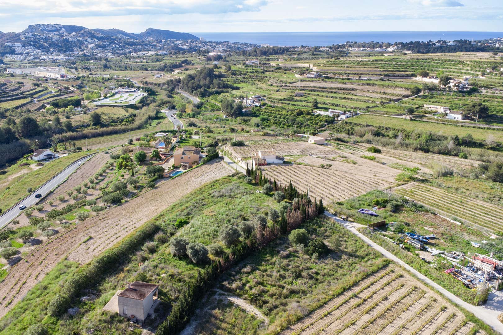 Luftaufnahme des weitläufigen, 10.920 m2 großen rustikalen Grundstücks in Teulada-Moraira mit terrassiertem Gelände und Blick auf das ferne Mittelmeer.