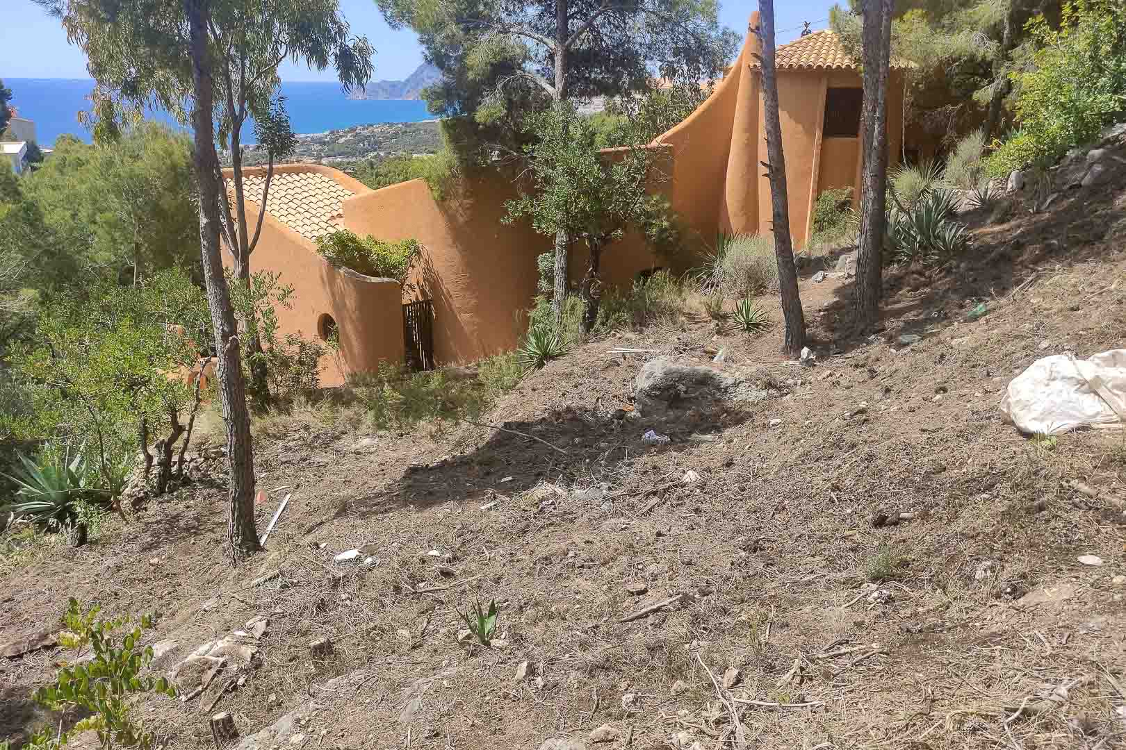 Außenansicht der Villa mit organischer Architektur und terrakottafarbenen Fassaden auf einem Hanggrundstück mit Pinien und Panoramablick auf das Mittelmeer.