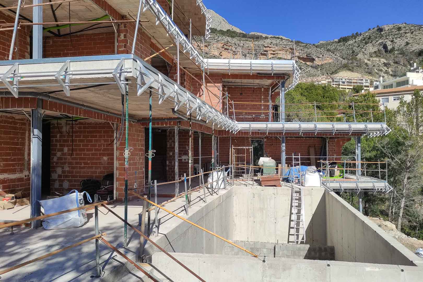 Baufortschritt der Villa in Altea mit Ziegelmauerwerk, Betonplatten und dem Rohbau des Pools vor der beeindruckenden Bergkulisse.