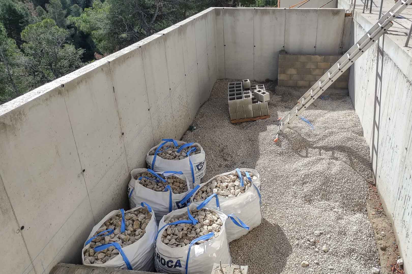 Baufortschritt mit Stahlbetonwänden, Fundamentkies und Baumaterialien, harmonisch eingefügt in die bewaldete Hügellandschaft von Altea.