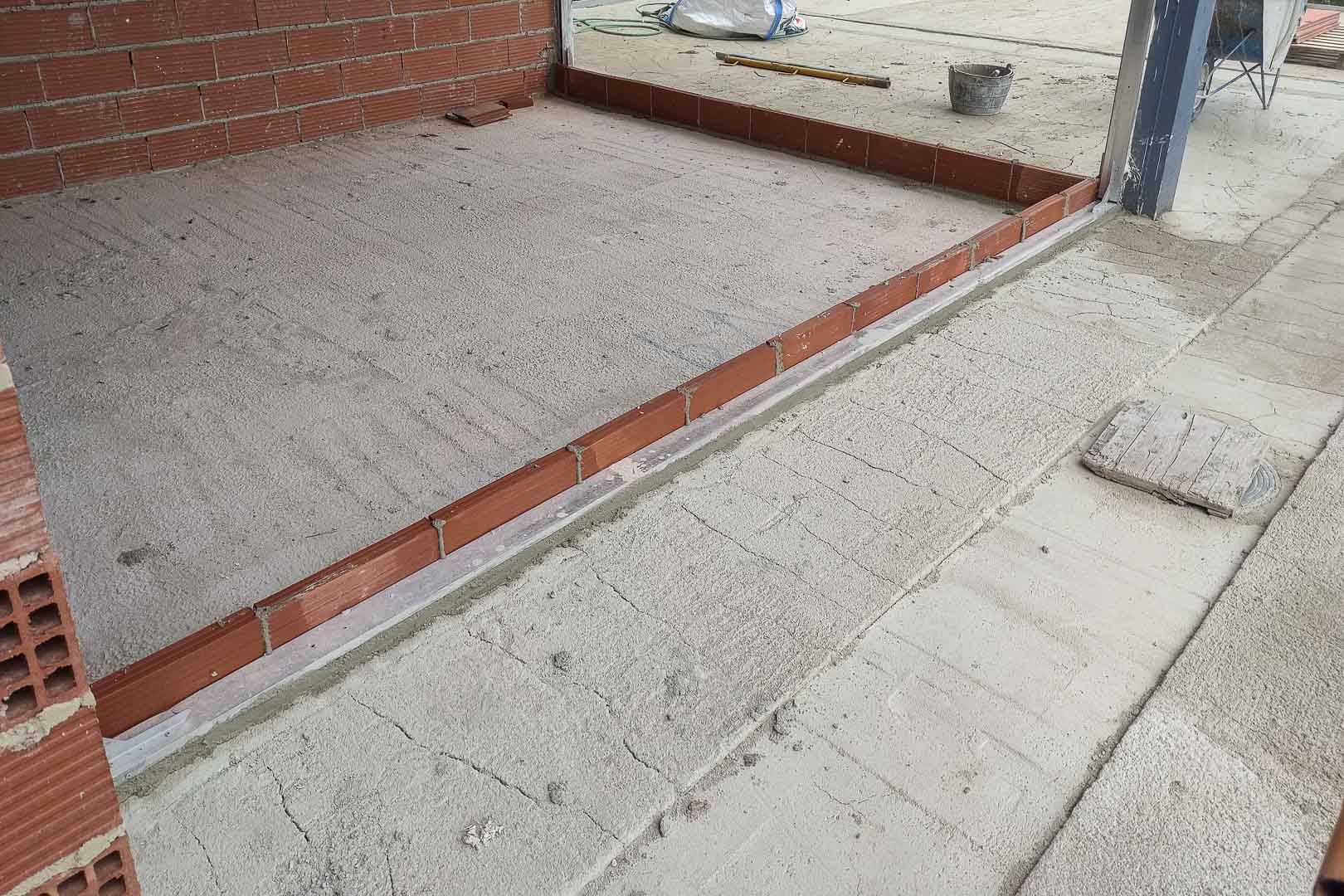 Bauphase: Detail der Bodenplatten-Nivellierung und Vorinstallation der Metallschienen für die großen Glasschiebetüren der Villa.