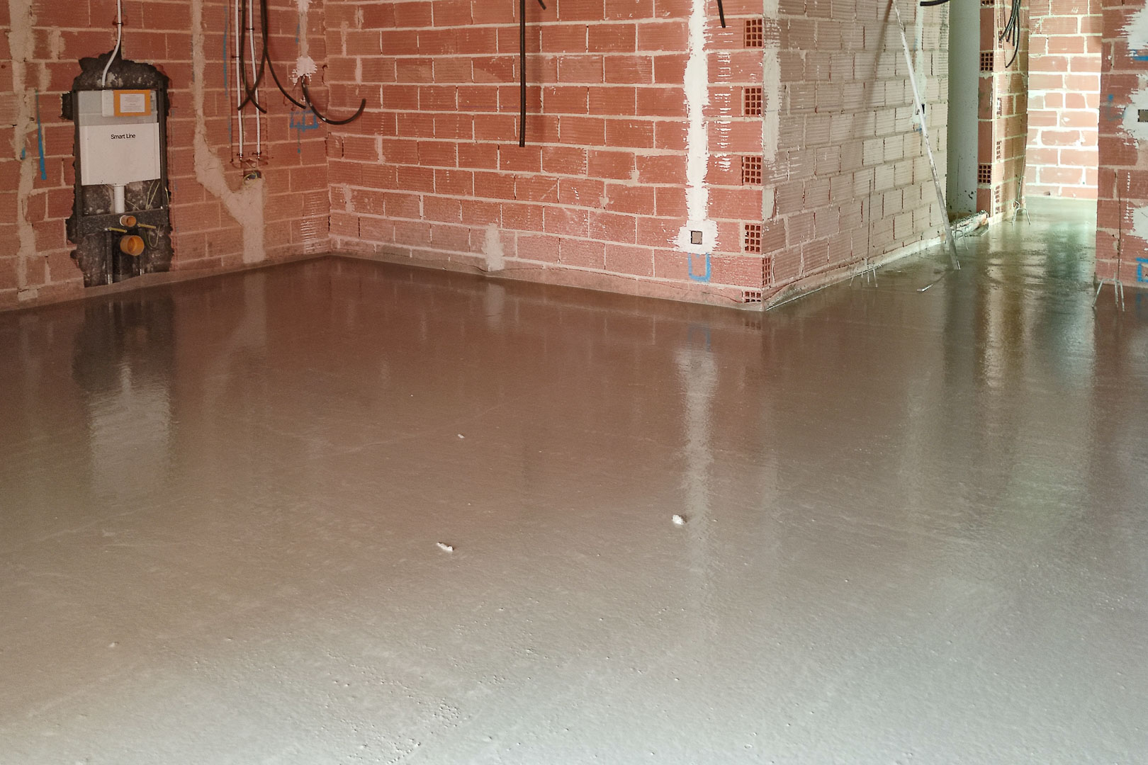 Bauphase mit frisch gegossenem Fließestrich. Sichtbares Mauerwerk und Vorwandinstallation für ein wandhängendes WC im Innenbereich der Villa.