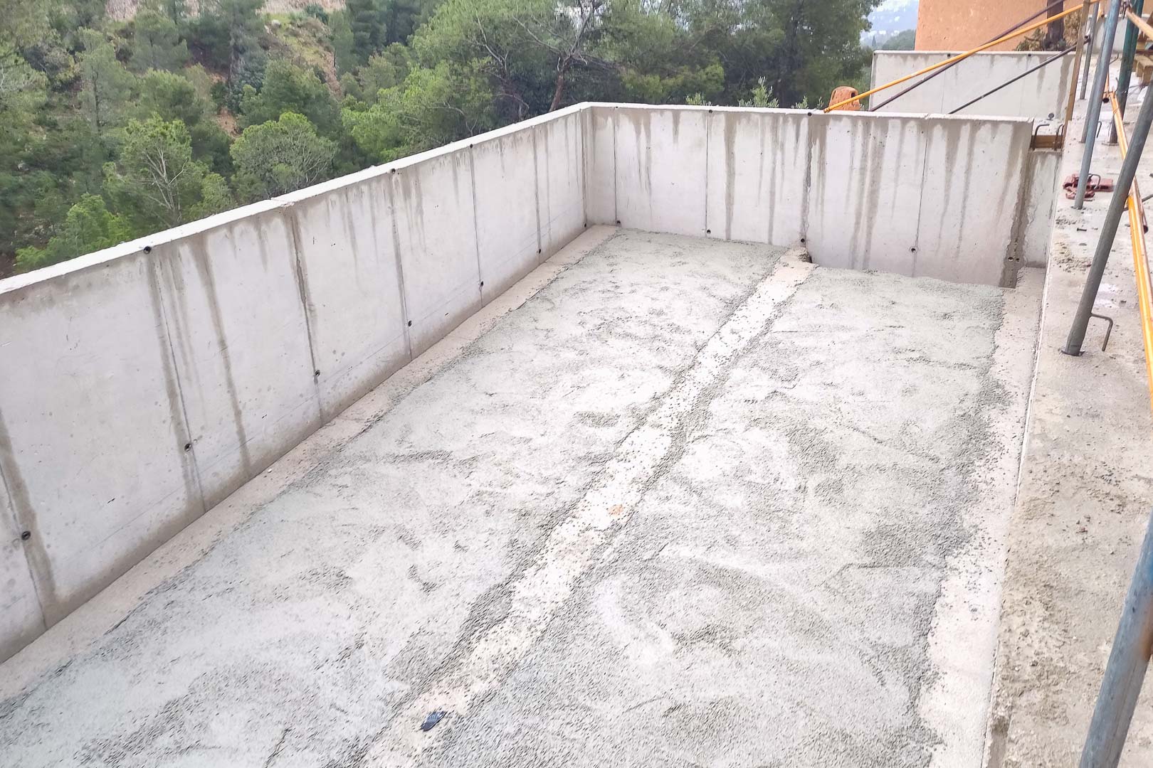 Stahlbetonkonstruktion in der Bauphase mit Umfassungsmauern und Bodenplatte für eine künftige Terrasse mit Blick auf den Pinienwald.