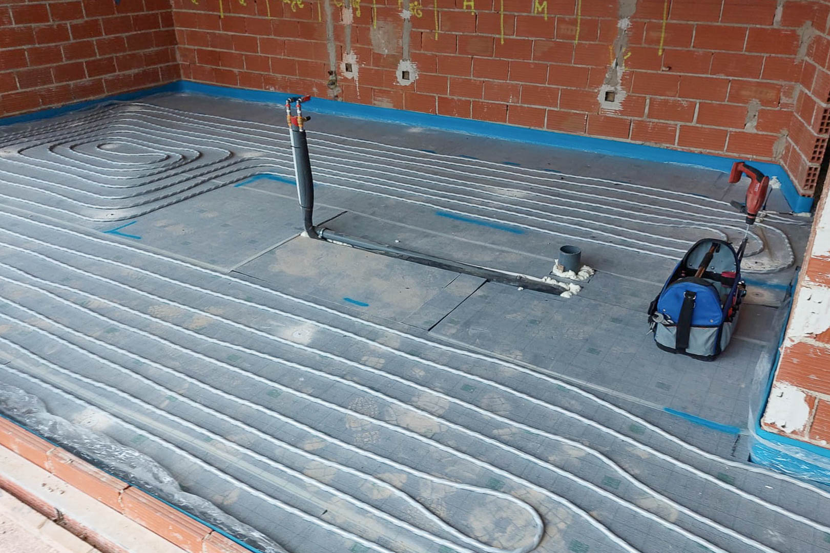 Technische Installation der Fußbodenheizung mit verlegten Heizrohren auf Dämmplatten in einem Raum im Rohbauzustand mit sichtbaren Ziegelwänden.