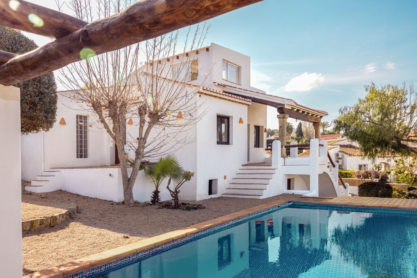 Ansicht der Villa mit türkisfarbenem Pool und weißer Fassade. Mediterranes Design mit Kiesgarten.