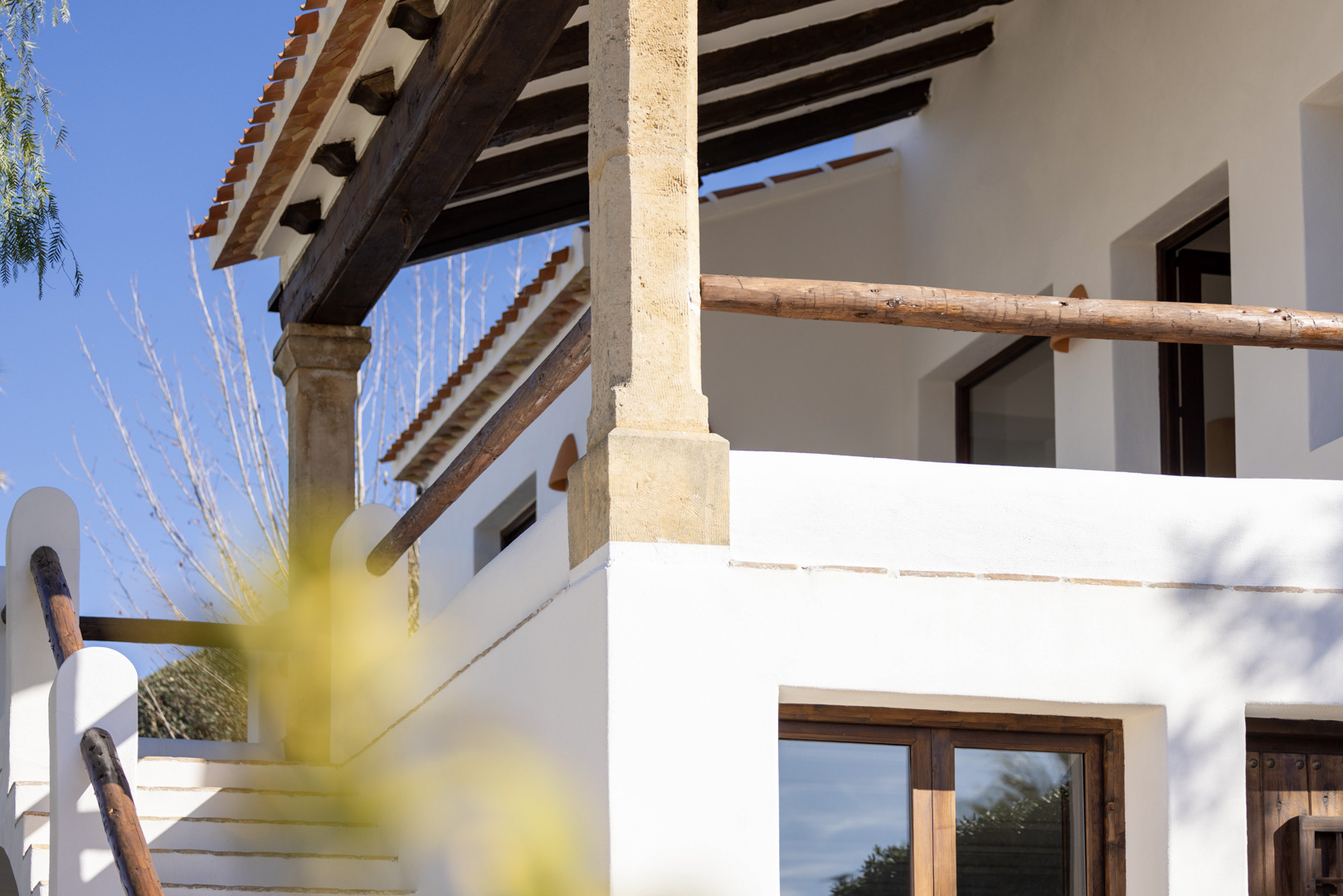 Architektonisches Detail der Villa: Veranda mit Holzbalken und rustikalem Geländer, weiße Steinaussentreppe.