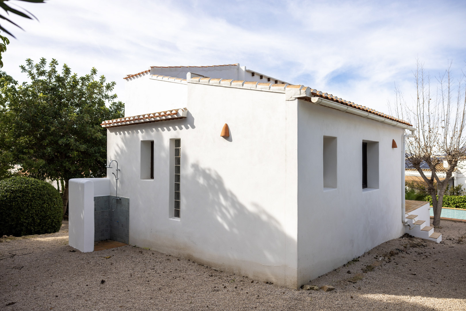 Außenansicht der Villa mit gefliester Außendusche und minimalistischer weißer Fassade mit Fenstern.