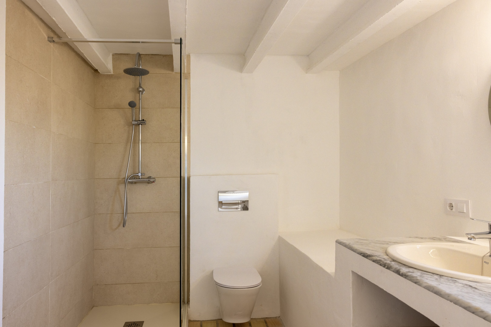 Badezimmer mit cremefarbener, gefliester ebenerdiger Dusche, weißer Toilette und Waschbecken mit Marmorplatte.