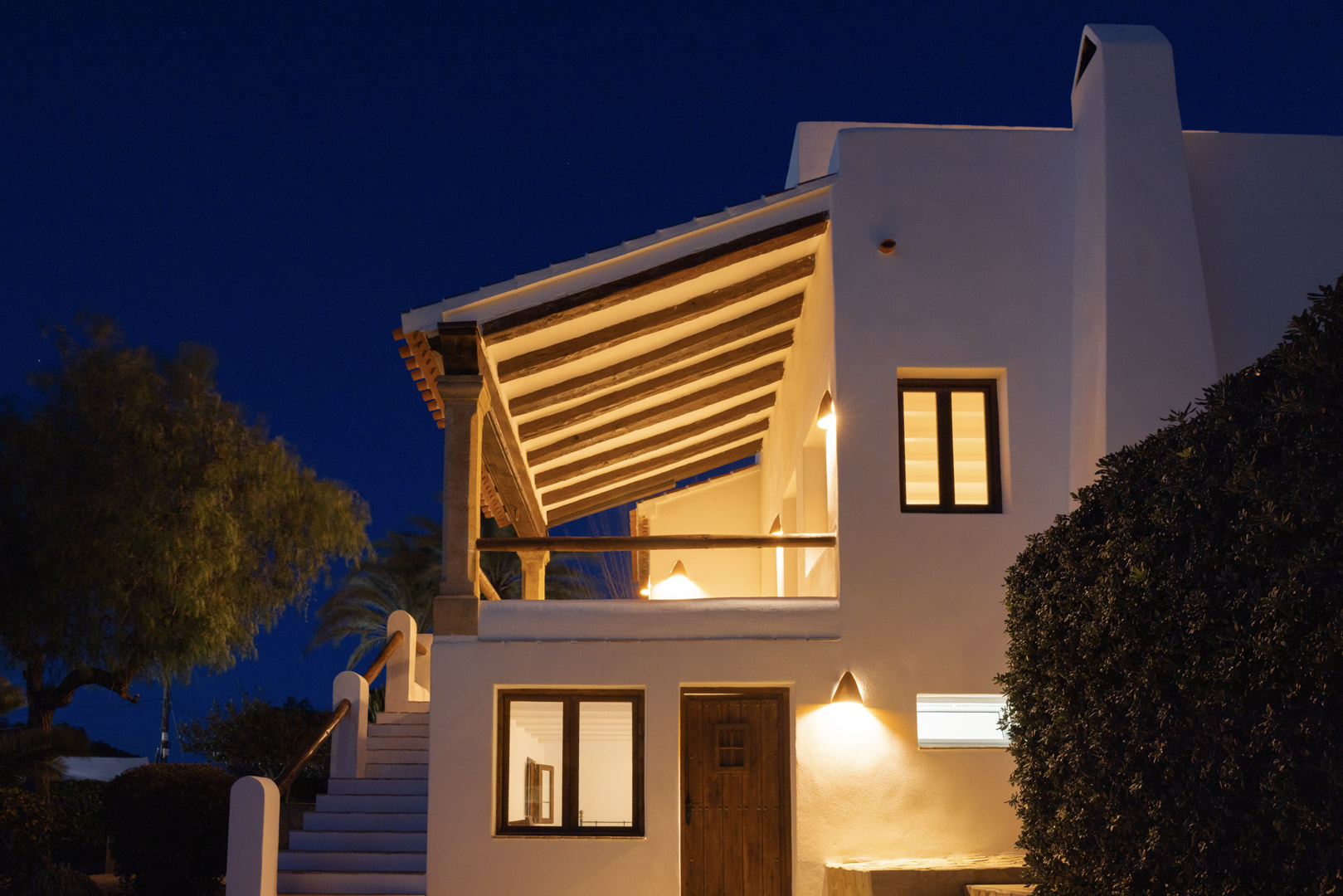 Beleuchtete Fassade der Villa in Tosalet, Jávea. Mediterrane Architektur mit überdachter Terrasse und Holzdetails.