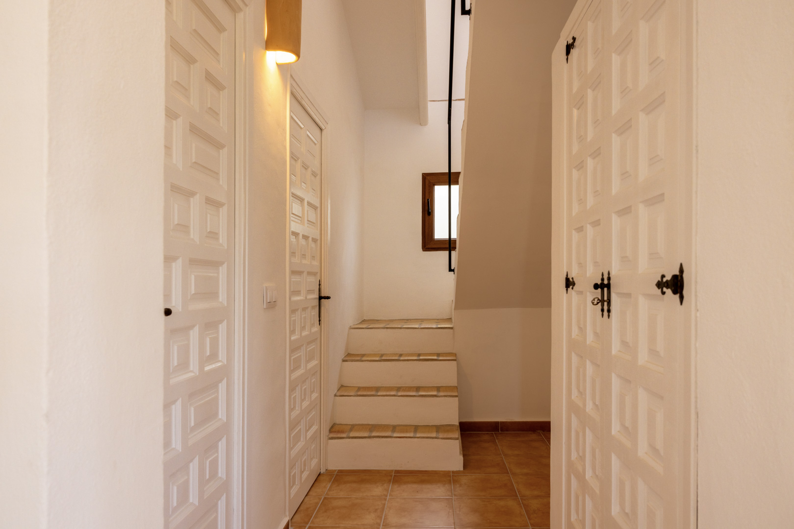 Detail des Flurs mit gefliester Treppe und weißen Holztüren mit geometrischem Design.