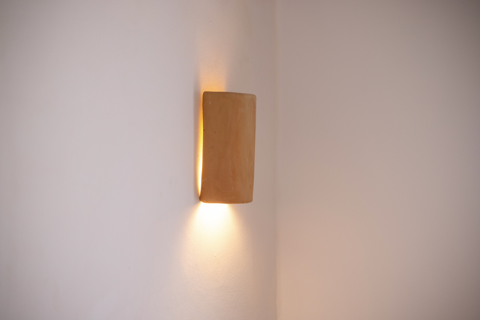 Detail einer rustikalen Wandleuchte, die warmes Licht in einem minimalistischen Interieur ausstrahlt.