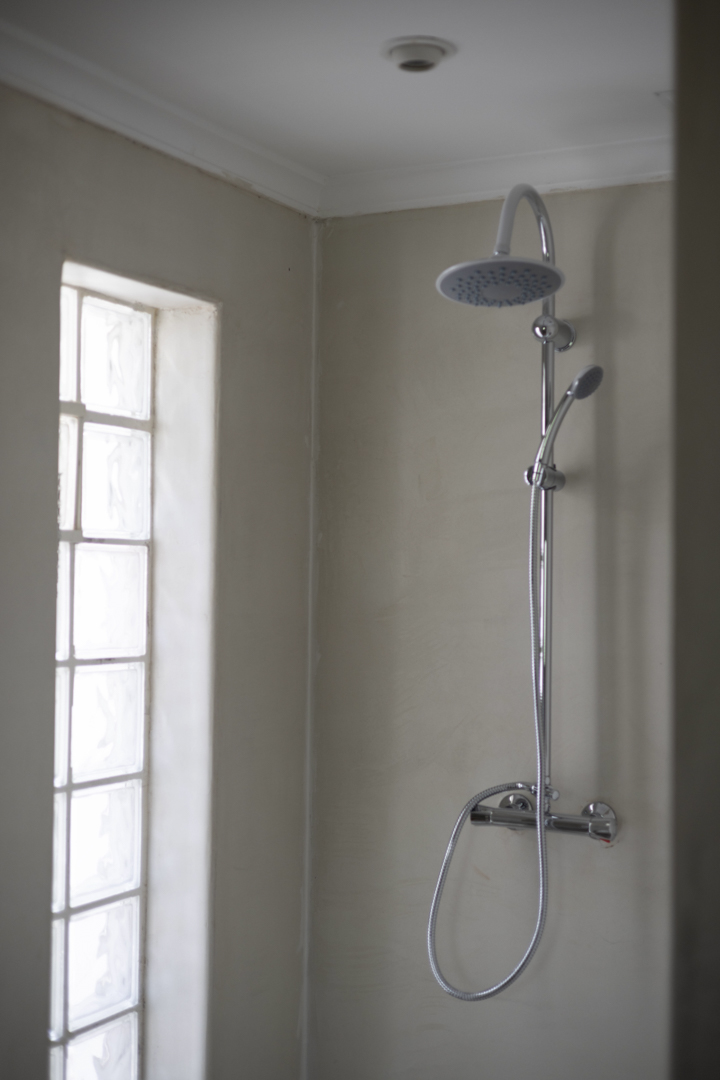 Duschdetail mit Regenkopf und Glasbausteinfenster in einem Badezimmer mit cremefarbenen Wänden.