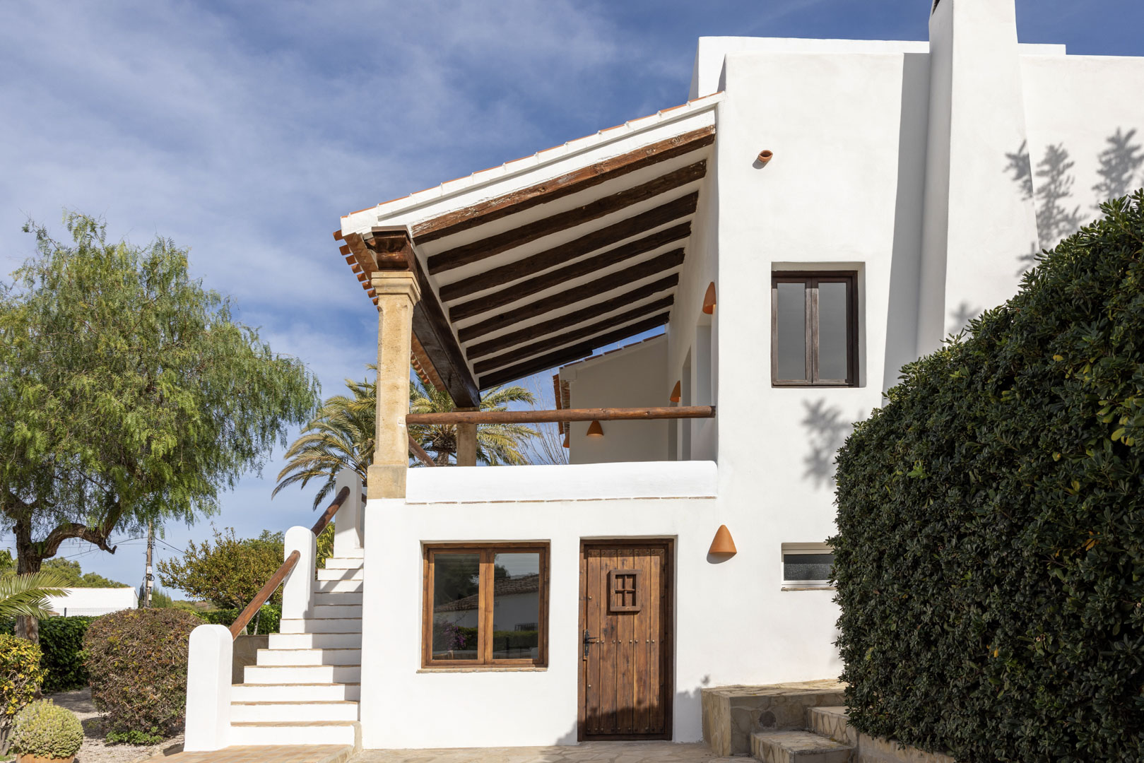 Fassade einer mediterranen Villa mit Veranda mit Holzbalken und gestuftem Zugang zum Garten.