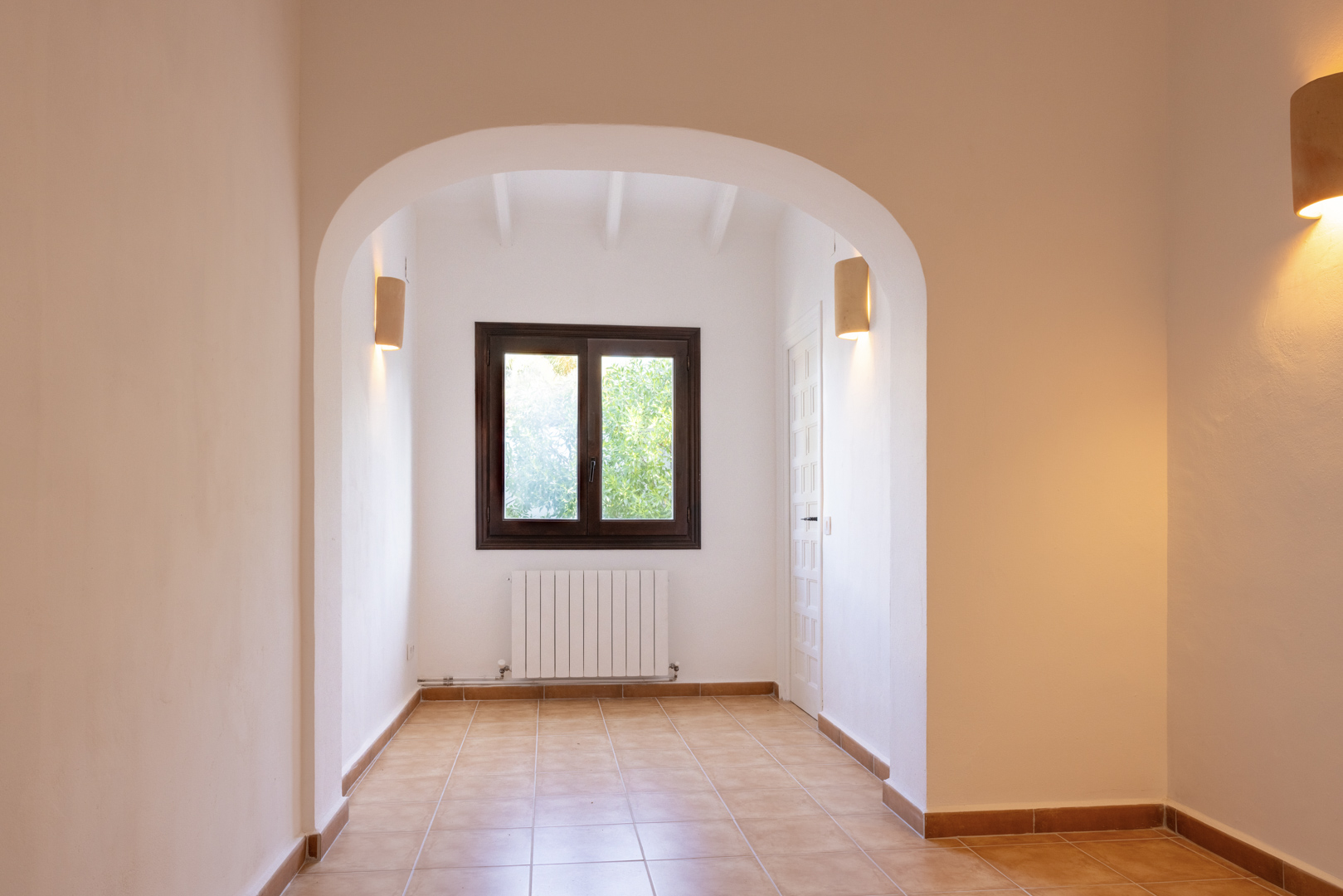 Helles Interieur mit architektonischem Bogen, Keramikfliesenboden und Fenster mit dunklen Holzrahmen.