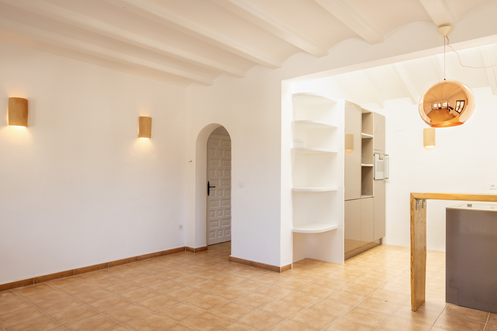 Helles Interieur mit weißen Regalen und offener Küche. Eine kupferfarbene Kugelleuchte hängt darüber.