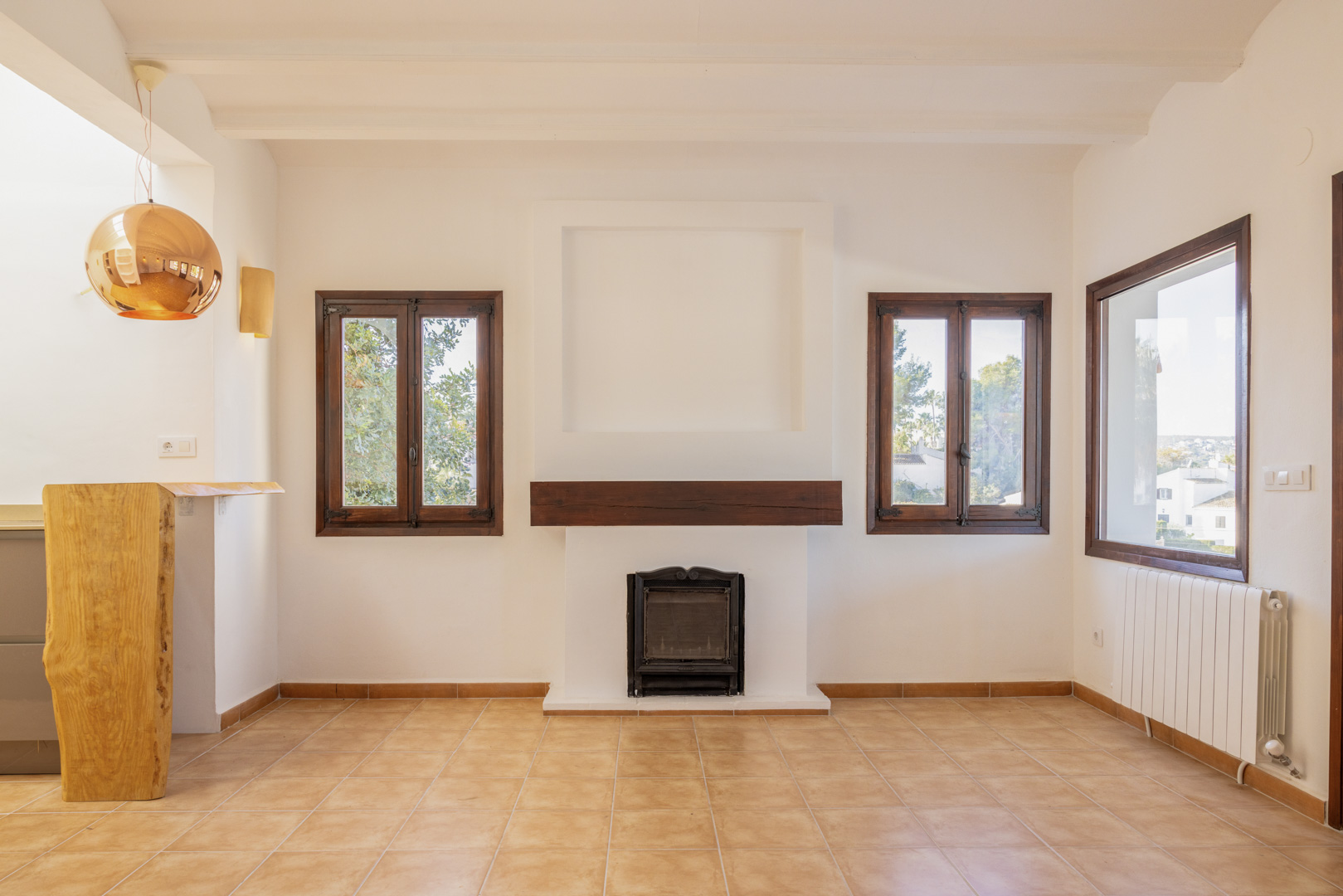 Helles Wohnzimmer mit rustikalem Kamin, Holzfenstern und Fliesenboden. Mediterranes Design mit modernen Akzenten.