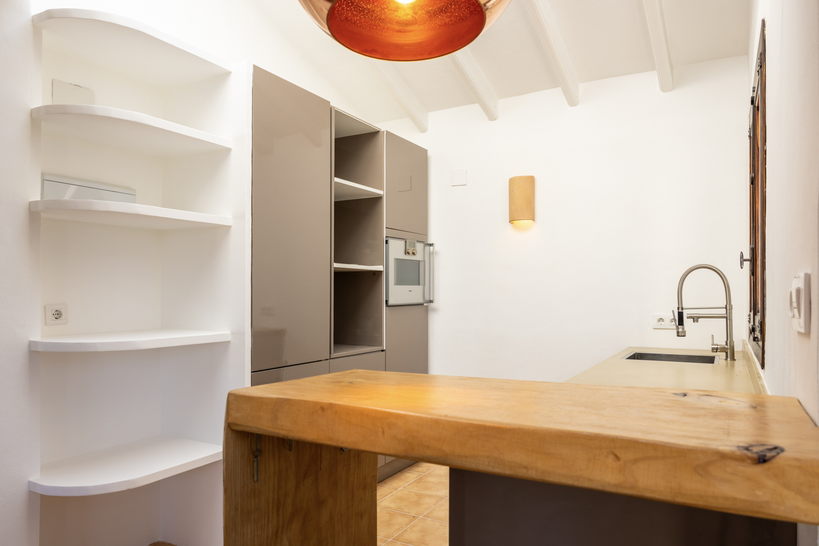 Küchendetail mit Holzinsel, weißen Regalen und warmer Beleuchtung.