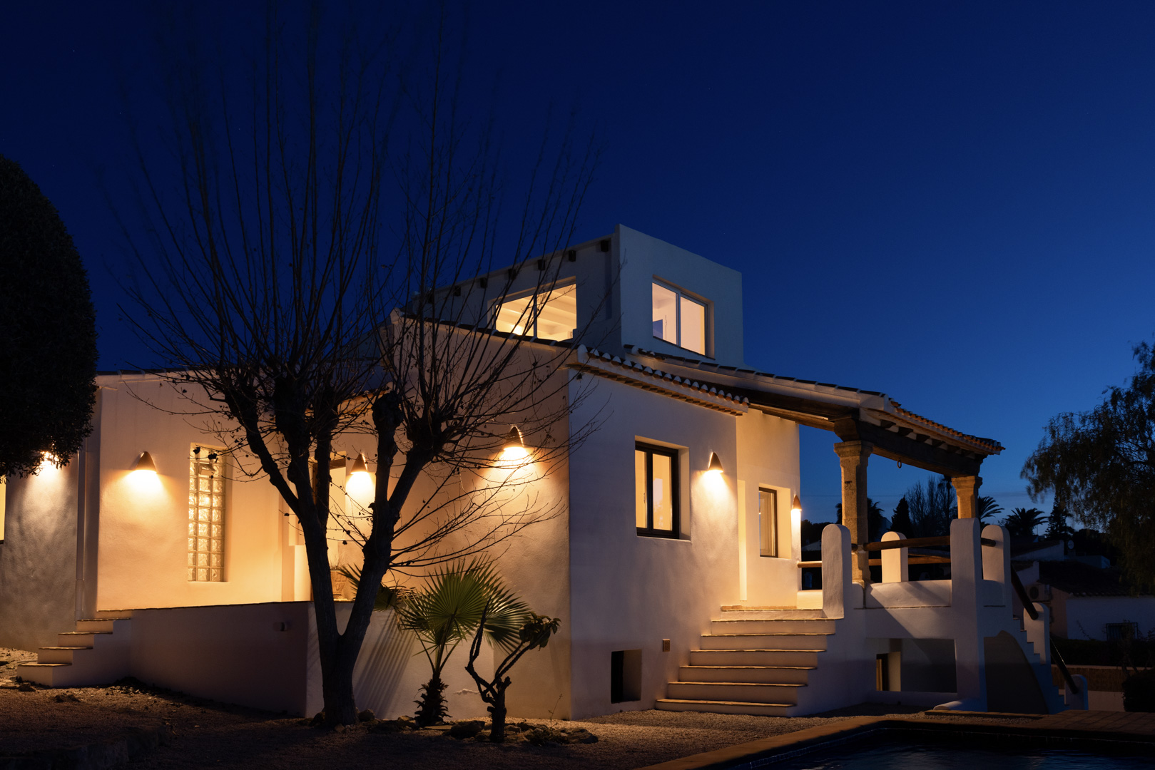 Nachtansicht der Villa mit beleuchteter weißer Fassade und Steindetails an der Veranda.