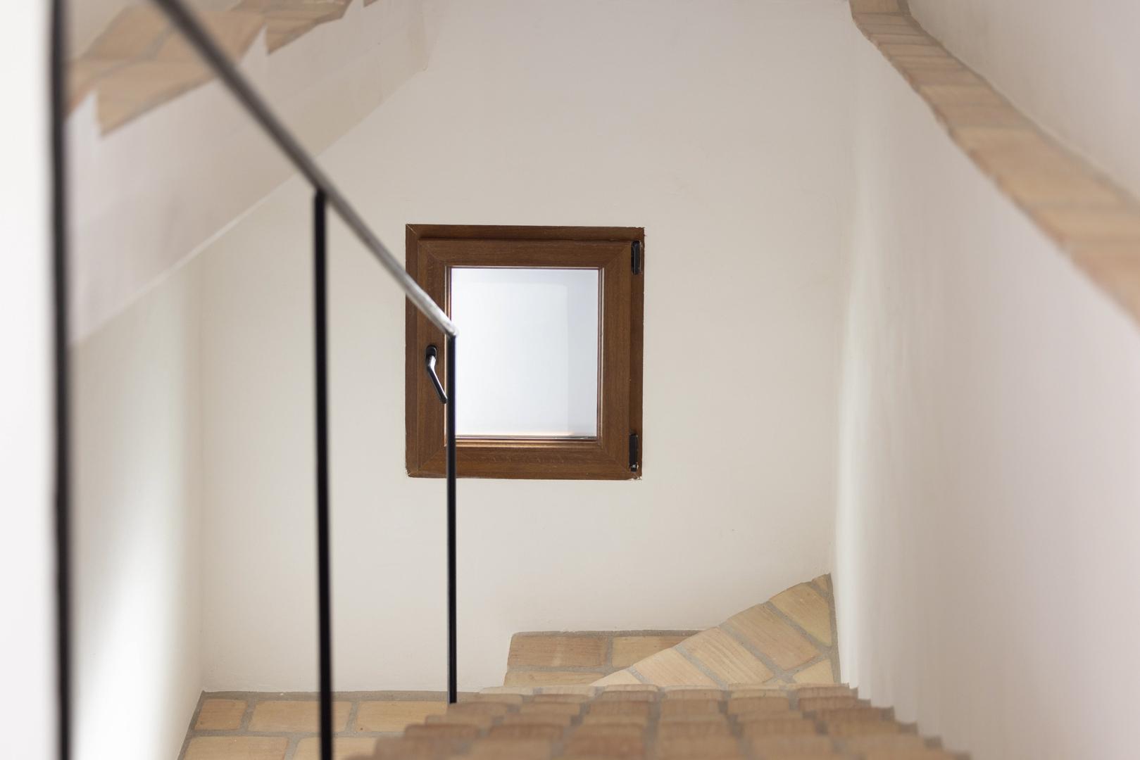 Treppendetail mit schwarzem Geländer und Holzfenster in weißer Wand.