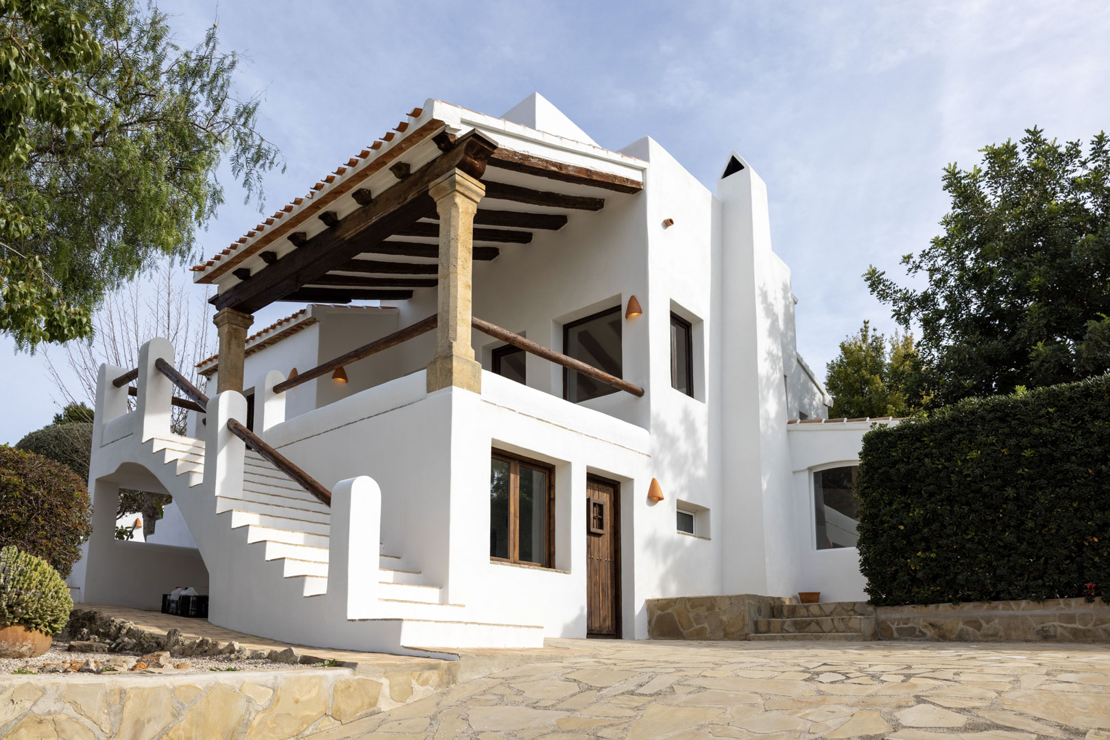 Villa-Fassade in Jávea mit überdachter Terrasse, Steinsäulen und Zugang über Außentreppe.