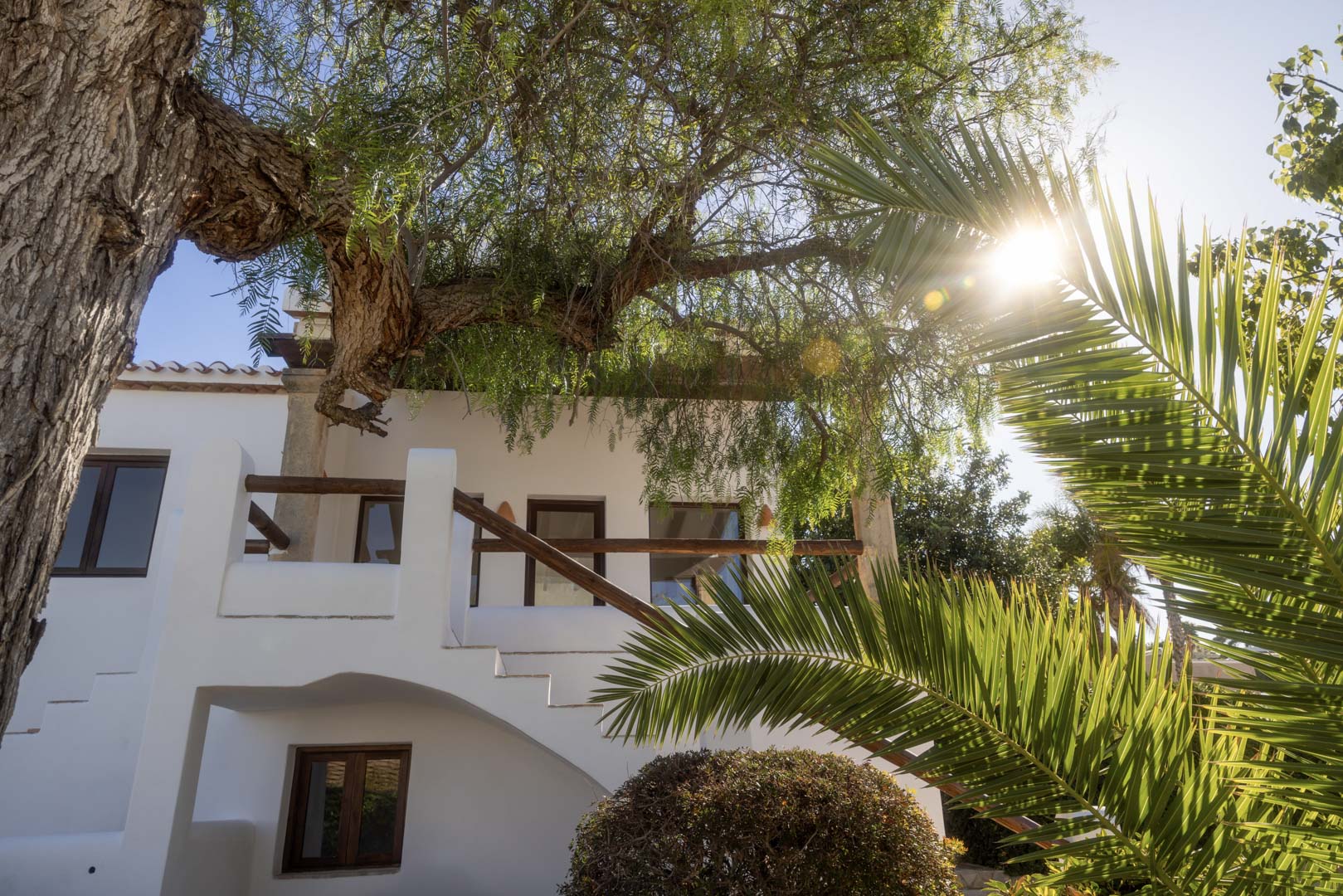 Weiße Fassade mit Holzbalkon und üppigem Grün, die die mediterrane Architektur hervorhebt.
