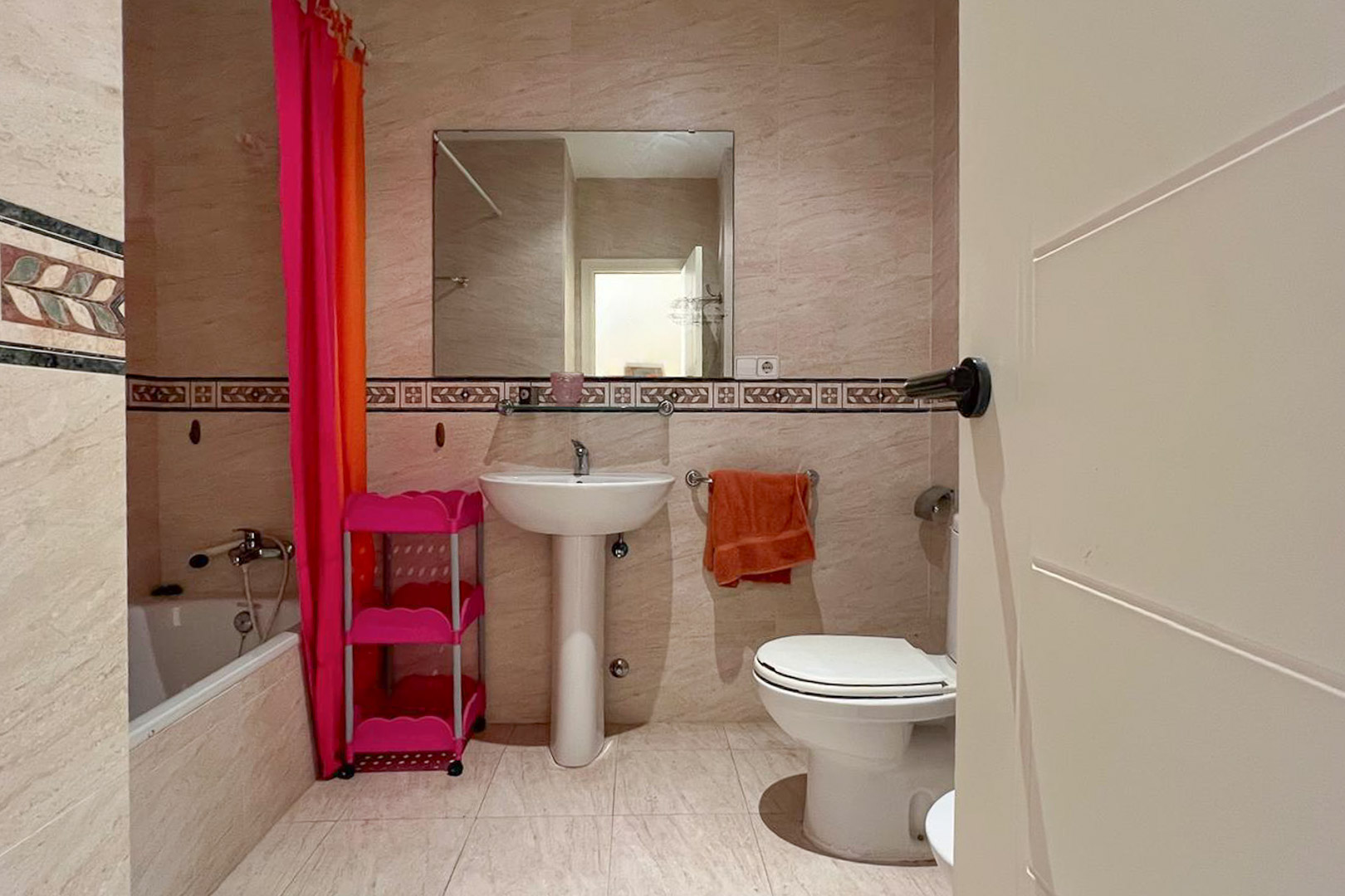 Badezimmer mit cremefarbenen Fliesen, weißem Waschtisch und dekorativen Wandakzenten.