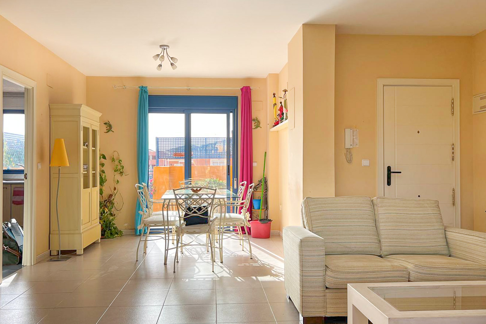 Helles Wohn-Esszimmer mit Balkon, Esstisch aus Metall und neutral gestreiftem Sofa.