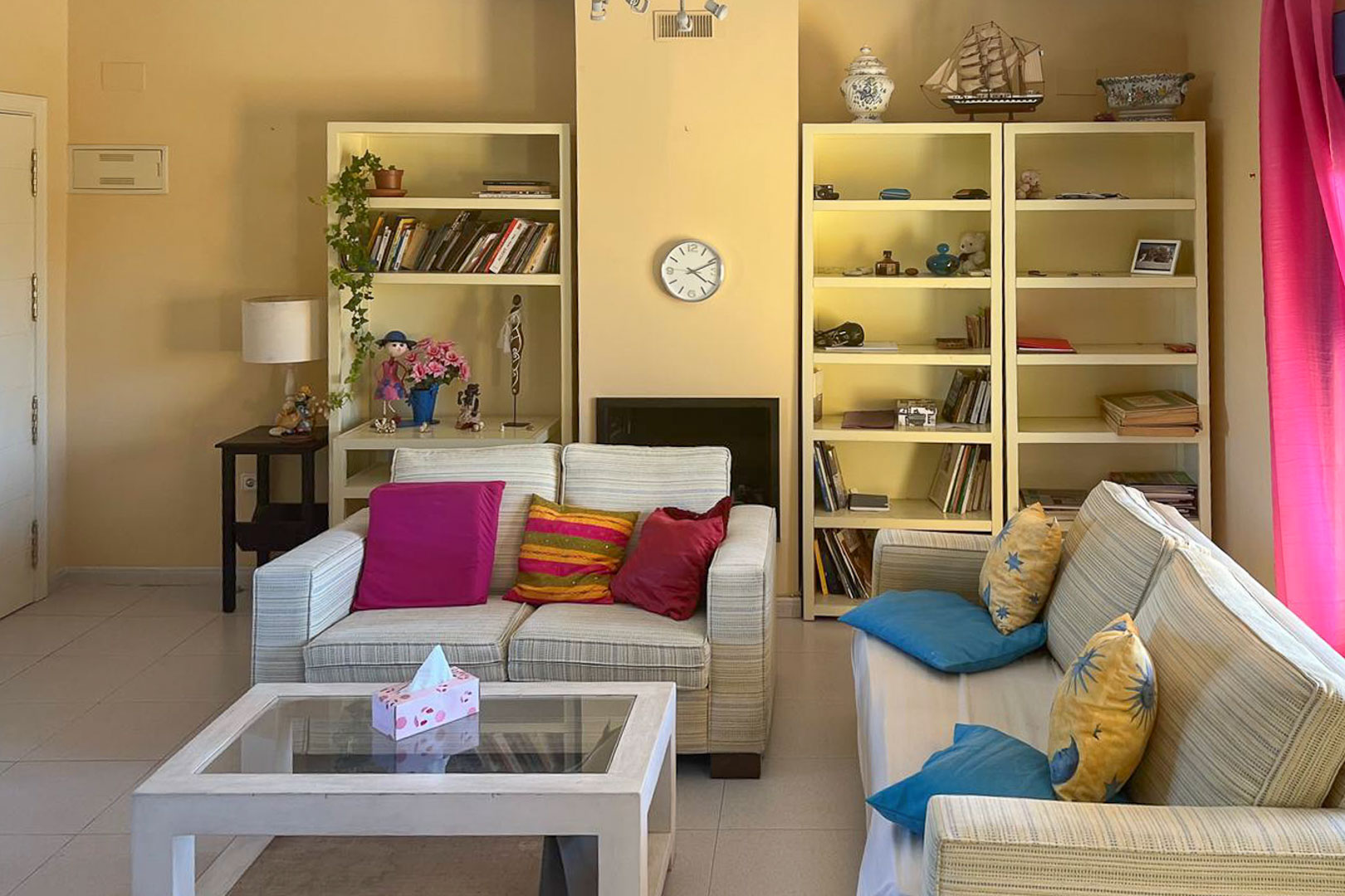 Helles Wohnzimmer mit cremefarbenen Bücherregalen, gestreiften Sofas und einem Couchtisch aus Glas.