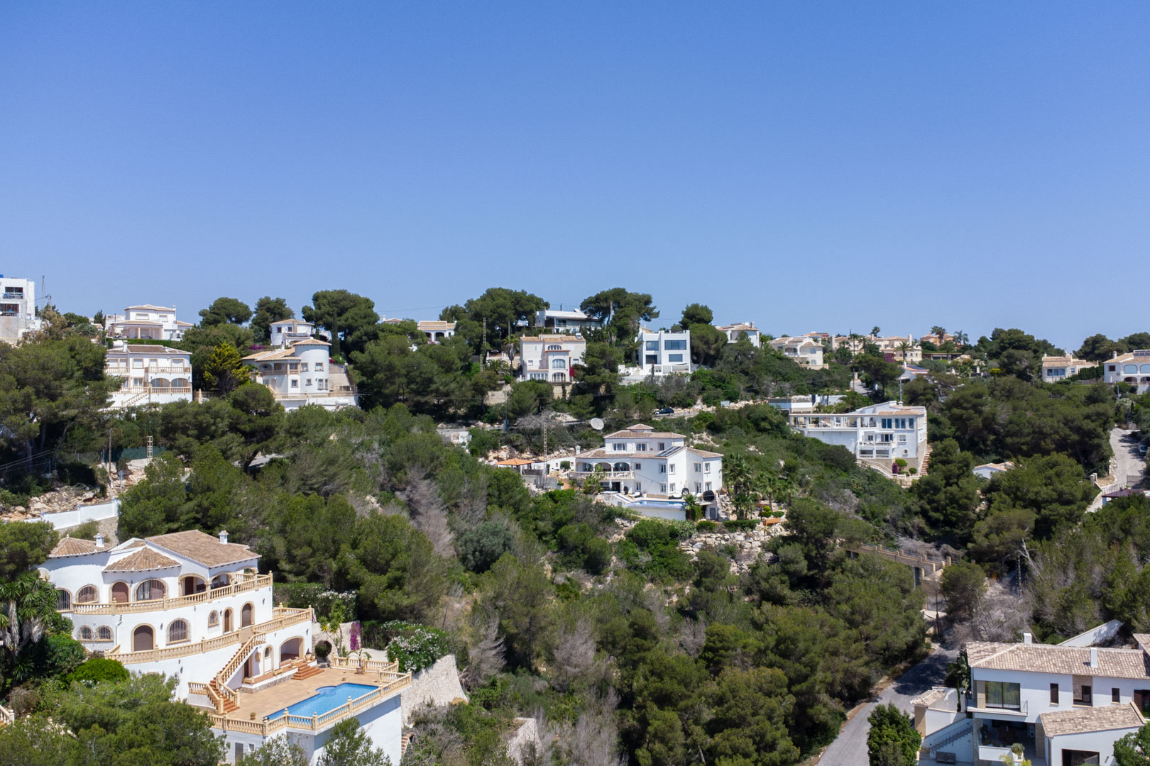 Erhöhte Ansicht des Wohngebiets Costa Nova in Jávea mit mediterranen Villen und privaten Pools, eingebettet in einen bewaldeten Pinienhang.