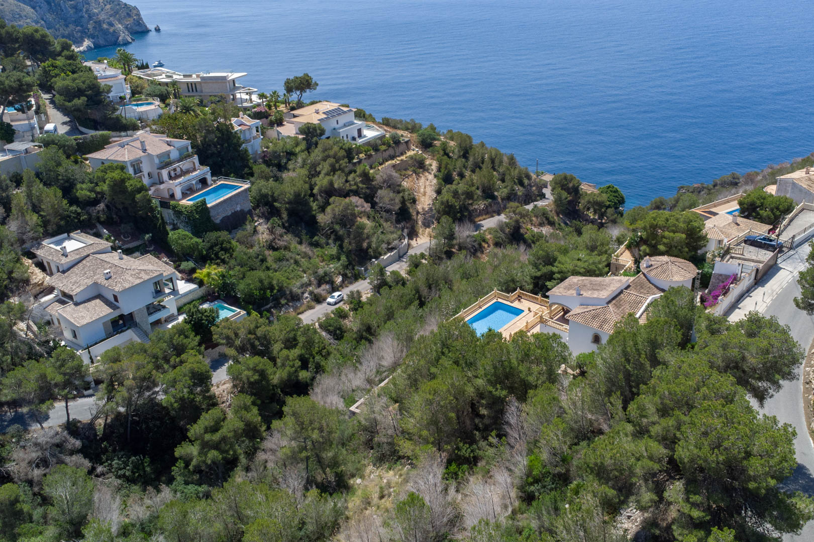 Luftaufnahme der Küste von Jávea mit mediterranen Villen inmitten von Pinien und dem blauen Meer, die die exklusive Lage der Grundstücke am Wasser verdeutlicht.
