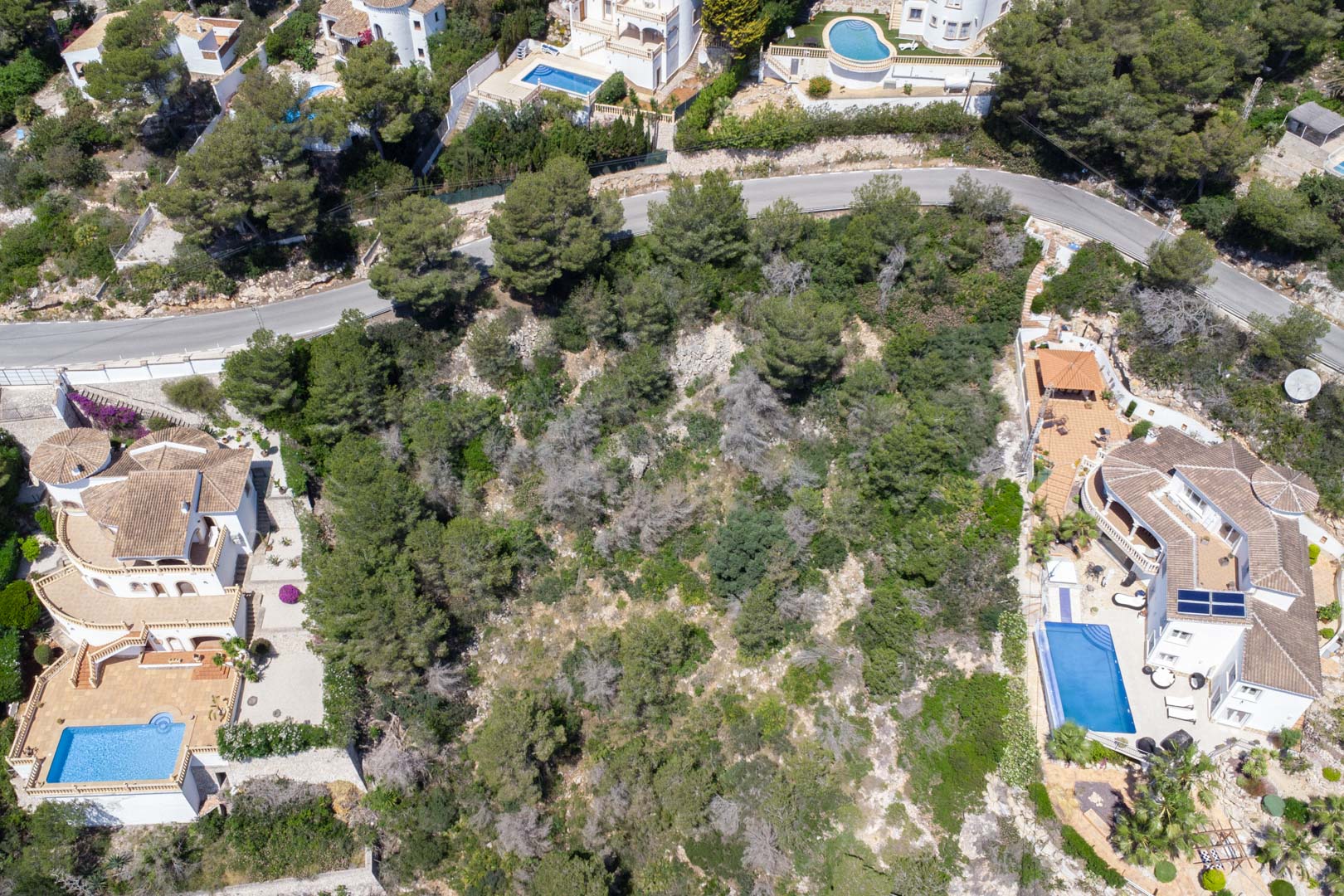 Luftaufnahme des abfallenden Grundstücks mit mediterraner Vegetation, gelegen zwischen bestehenden Villen mit privaten Pools in Costa Nova.