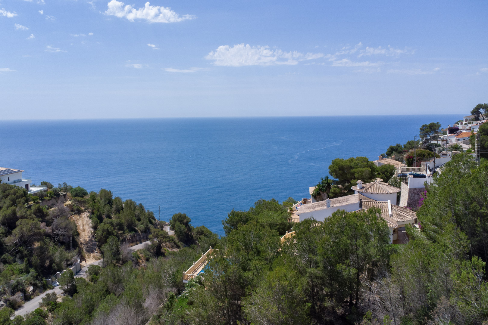 Panoramablick auf das Mittelmeer von der Anhöhe in Costa Nova, mit pinienbewachsenen Hängen und angrenzenden Wohnhäusern an der Küste von Jávea.