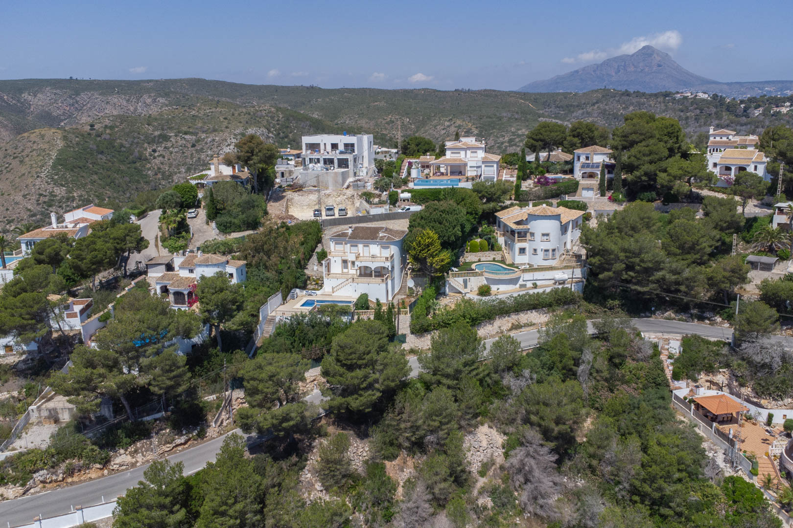 Luftaufnahme der Urbanisation Costa Nova in Jávea mit weißen Villen inmitten von Pinienwäldern und dem Berg Montgó im Hintergrund.