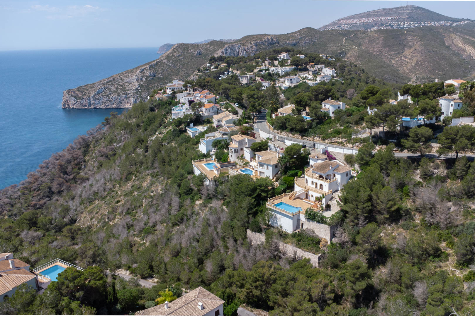 Luftaufnahme der Urbanisation Costa Nova in Jávea mit weißen Villen und privaten Pools, eingebettet in einen Pinienwald an der Mittelmeerküste.