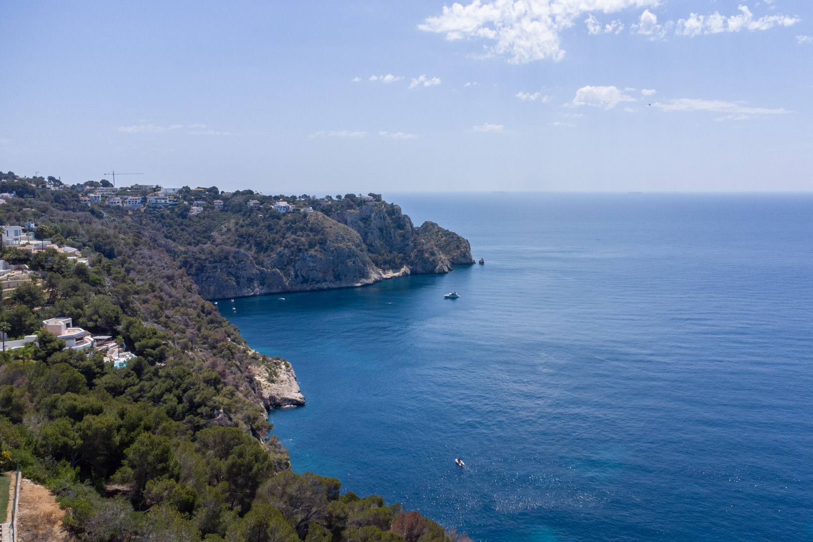 Luftaufnahme der zerklüfteten Küste von Jávea mit bewachsenen Klippen und weitem Blick über das tiefblaue Mittelmeer.