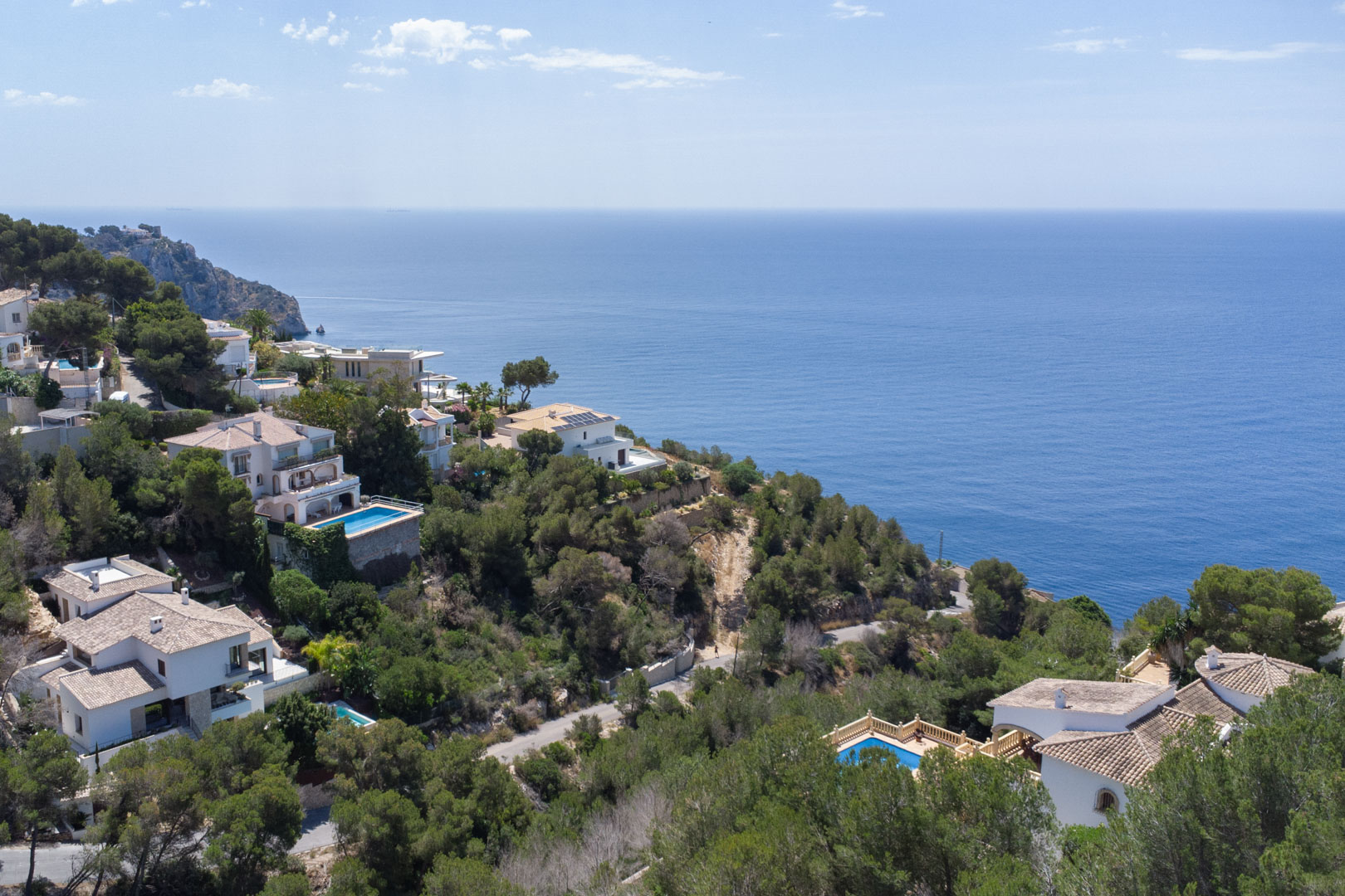 Luftbild der Küste von Jávea mit mediterranen Villen, privaten Pools und dichtem Pinienbewuchs vor dem weiten Panorama des Mittelmeers.