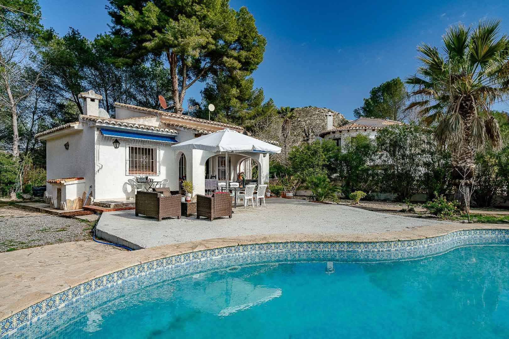 Außenansicht der Villa mit privatem Mosaikpool, großzügiger Terrasse und traditioneller Naya, eingebettet in einen Garten mit Pinien und Palmen.
