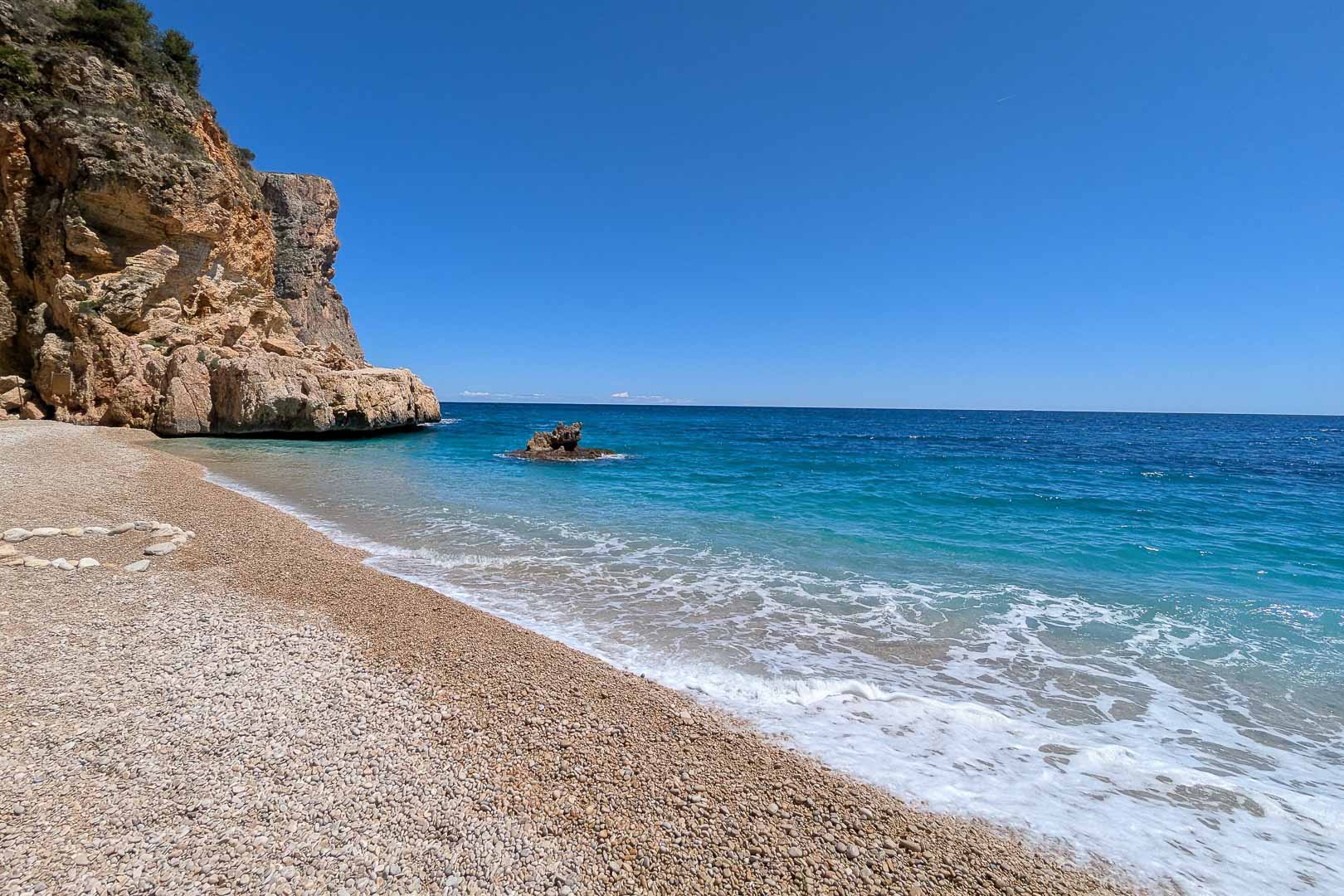 Cala Llebeig, eine naturbelassene Kieselbucht mit kristallklarem Wasser und markanten Felsklippen, direkt erreichbar von der Wohngegend La Arnella.