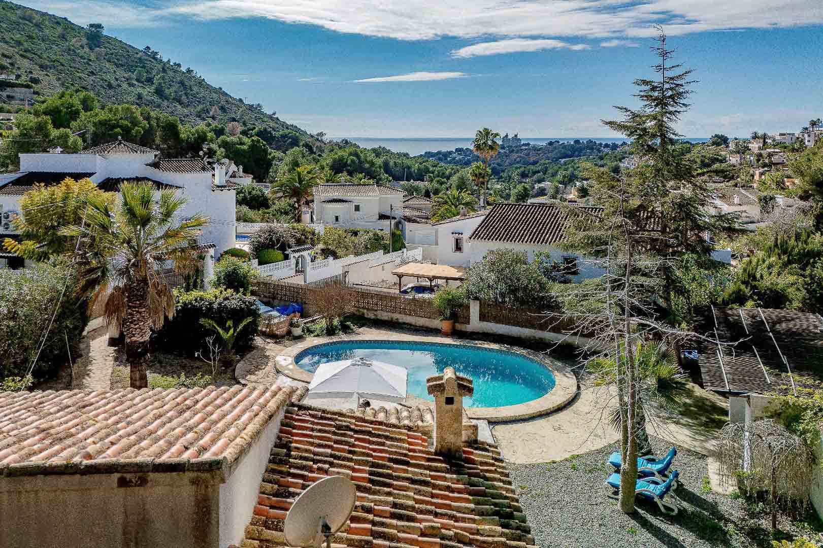 Erhöhte Ansicht des nierenförmigen Privatpools und des mediterranen Gartens mit weitem Blick auf das Meer und die umliegende Wohngegend von Moraira.