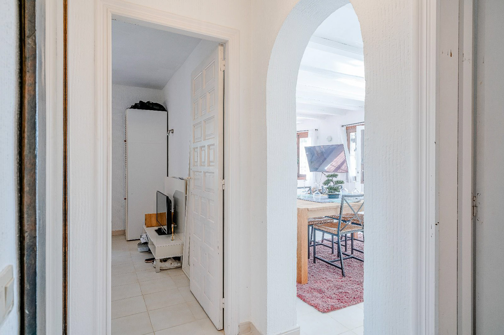 Flur mit mediterranem Rundbogen zum Esszimmer und weißer Paneeltür, die in ein helles Schlafzimmer mit hellen Fliesenböden führt.