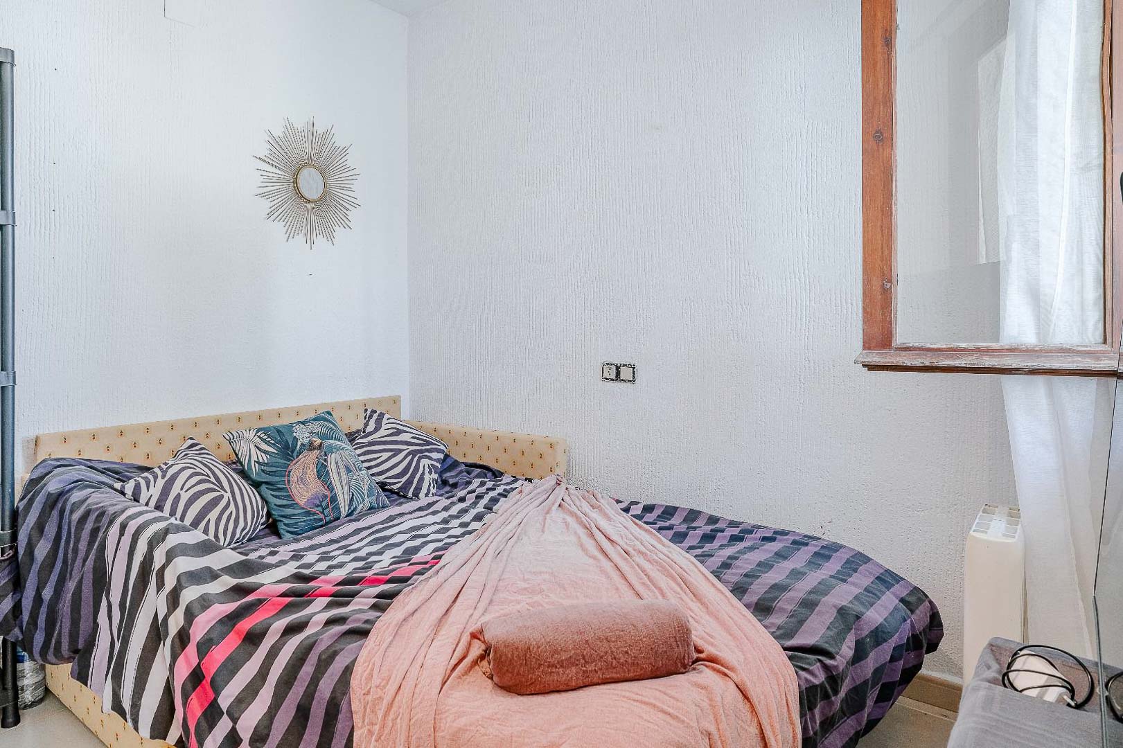 Helles Schlafzimmer mit strukturierten Wänden, Einzelbett mit gepolstertem Kopfteil und Holzfenster, das für natürliches Licht sorgt.