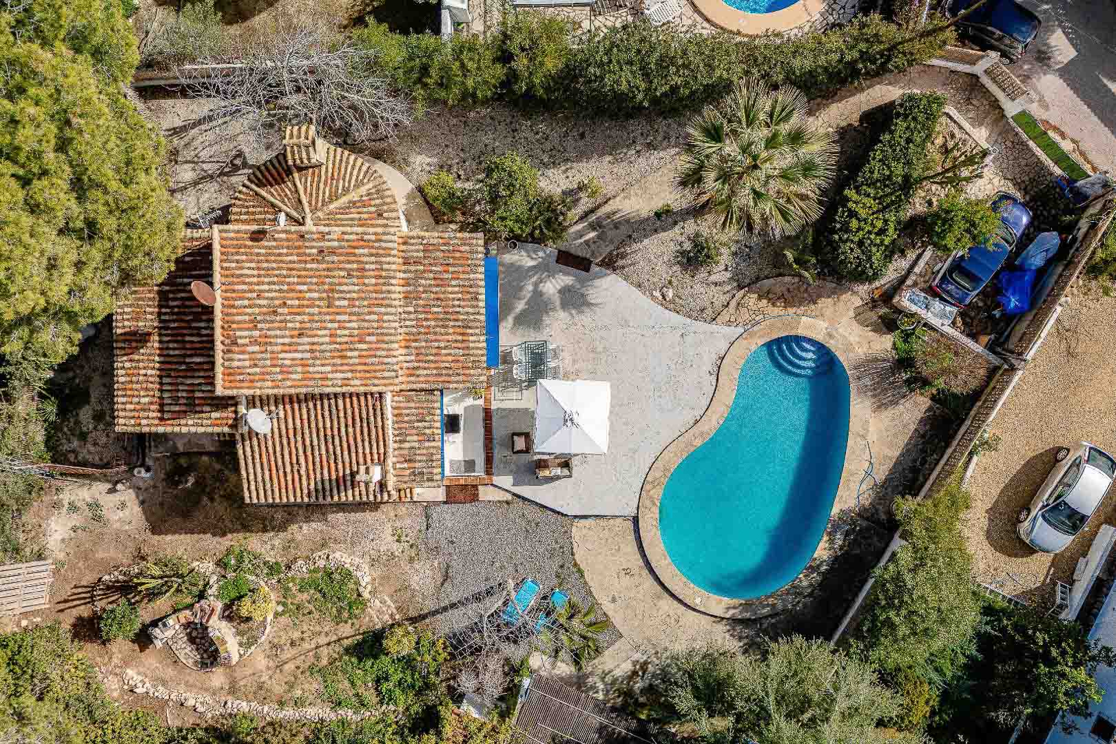 Luftaufnahme des Anwesens mit nierenförmigem Pool, befestigter Terrasse und traditionellem Ziegeldach inmitten eines mediterranen Gartens.