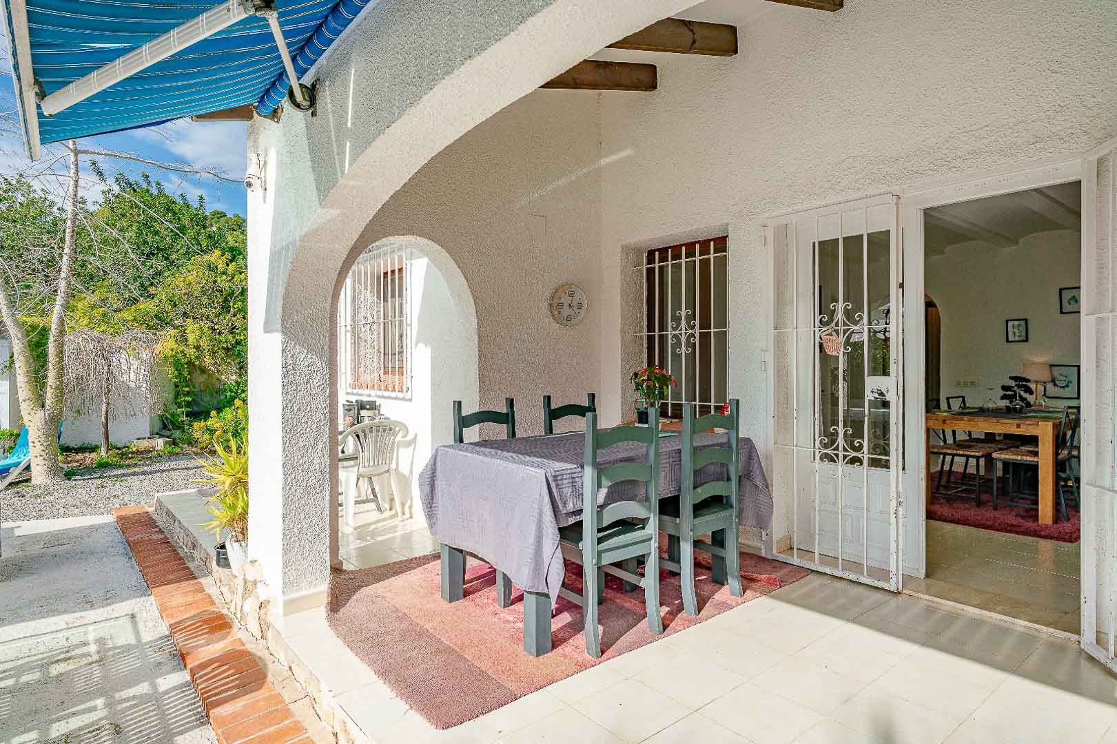 Überdachte Veranda mit mediterranen Rundbögen, Holzbalken und Essplatz im Freien. Der Bereich verbindet den Garten über gesicherte Türen mit dem Innenraum.