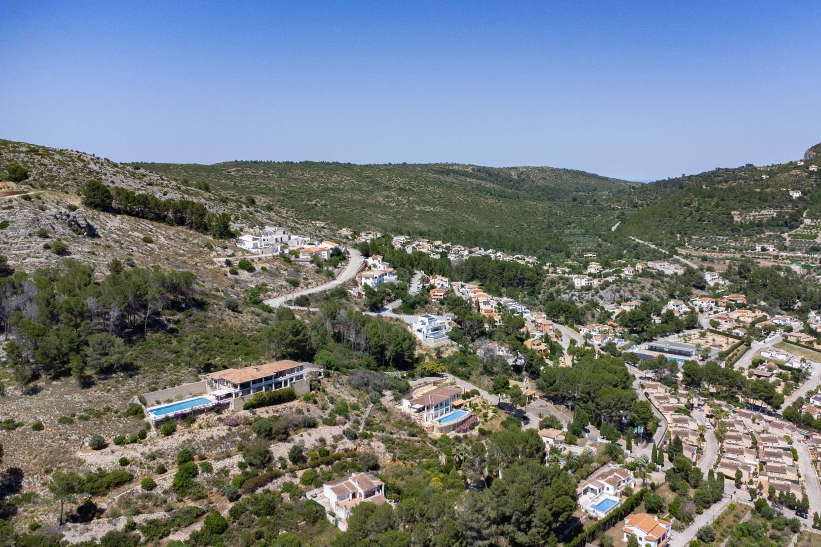 Luftaufnahme der Wohnanlage in Alcalalí, die die erhöhte Lage der Grundstücke und die Einbettung der Villen in die natürliche Landschaft des Tals zeigt.